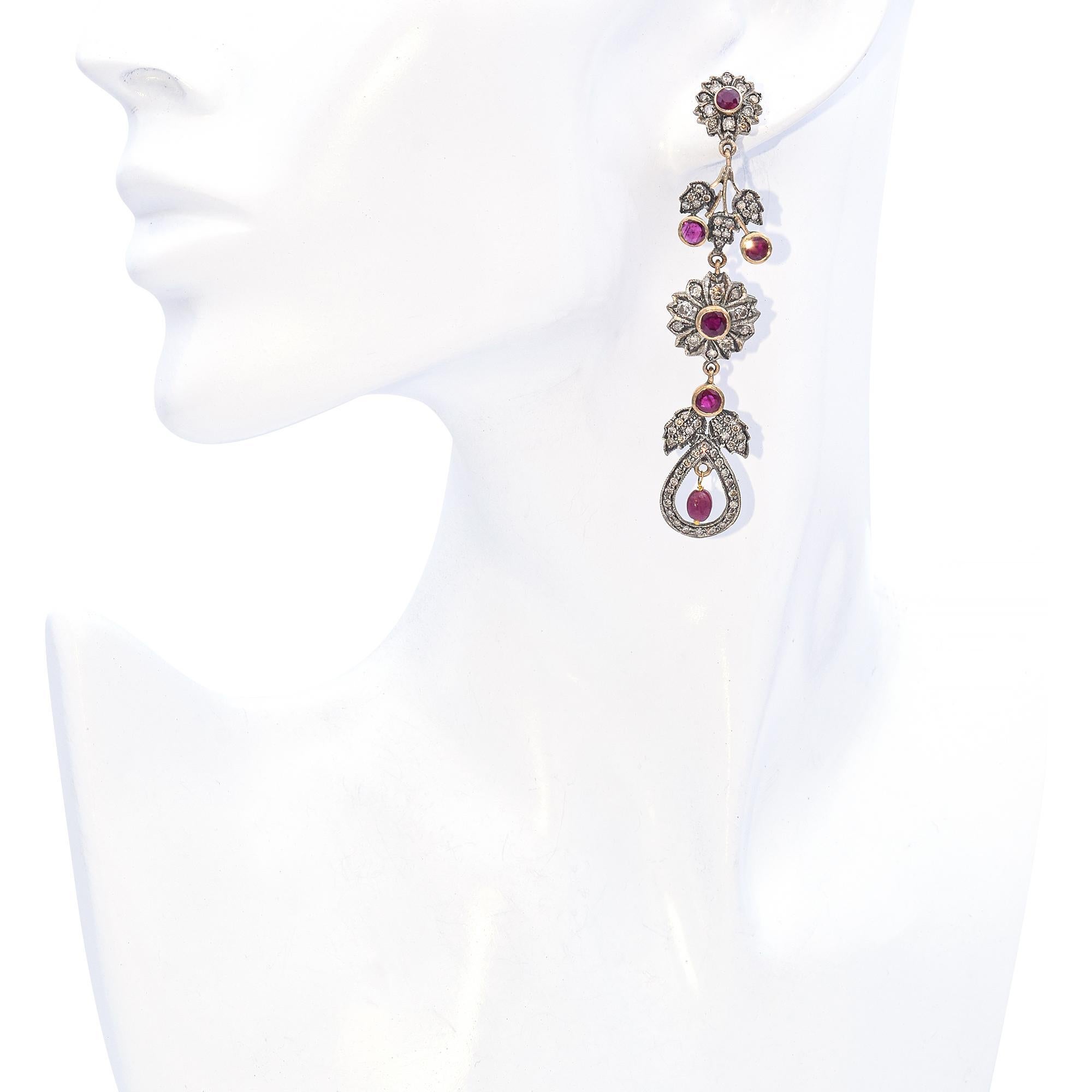 Crafted with intricate detail, these earrings feature a stunning combination of vibrant rubies and sparkling diamonds. The design showcases floral motifs with round rubies at the center, surrounded by a halo of shimmering diamonds. Dangling elements