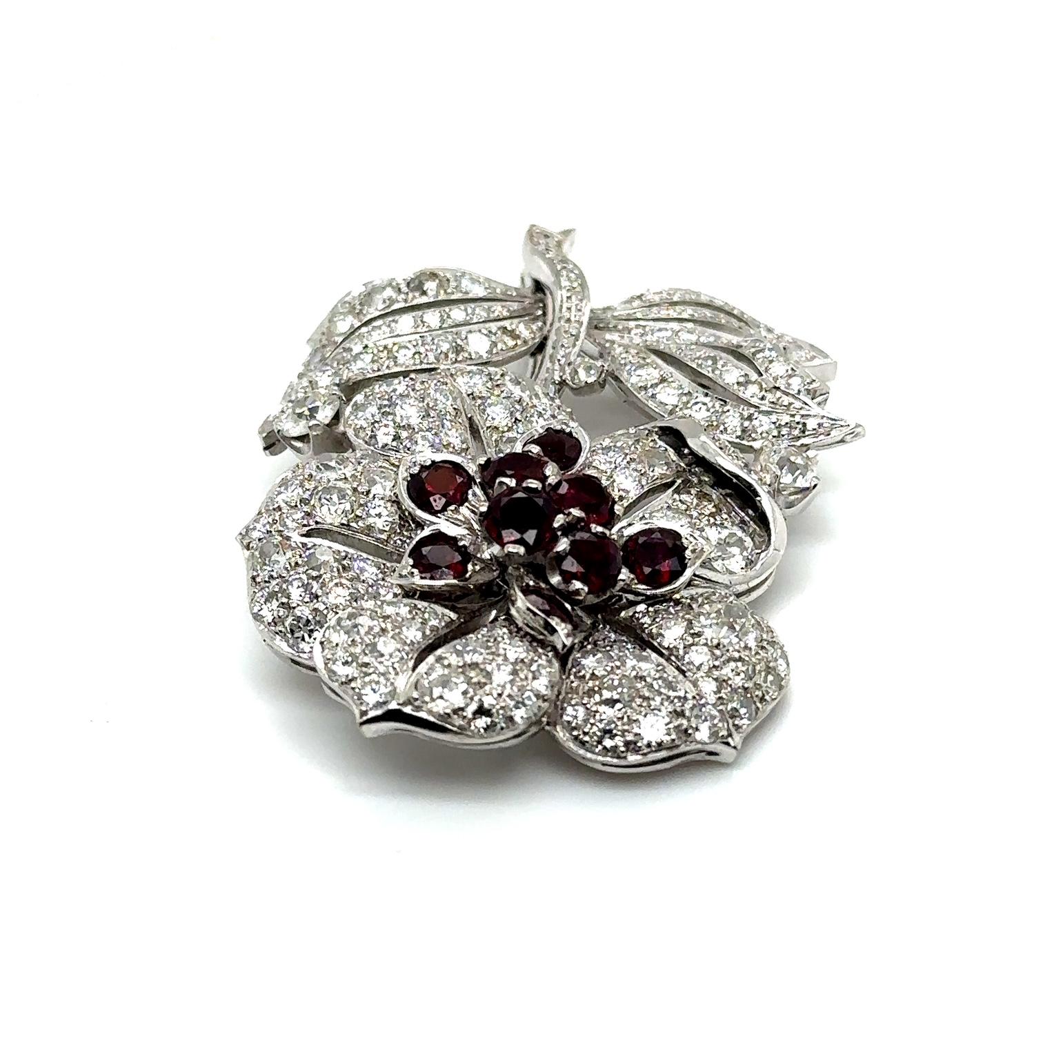 Introducing a timeless piece of elegance: the 18ct White Gold Large Ruby And Diamond Flower Brooch. Crafted circa 1960, this exquisite accessory exudes vintage charm and sophistication.
At its heart lies a radiant bouquet of nine stunning rubies,