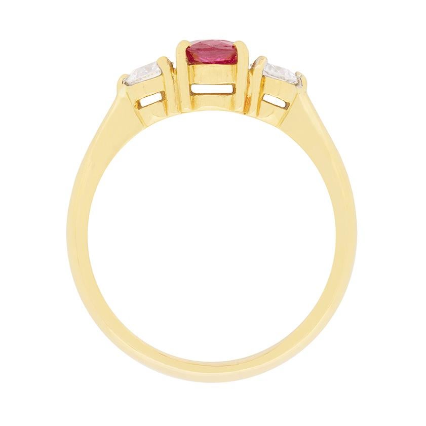 In the centre of this three stone ring is a wonderfully deep red ruby weighing 0.72 carat. It is a natural stone, set within an 18 carat yellow gold collet with claws. Adjacent on either side are two stunning diamonds, each weighing 0.25 carat. They