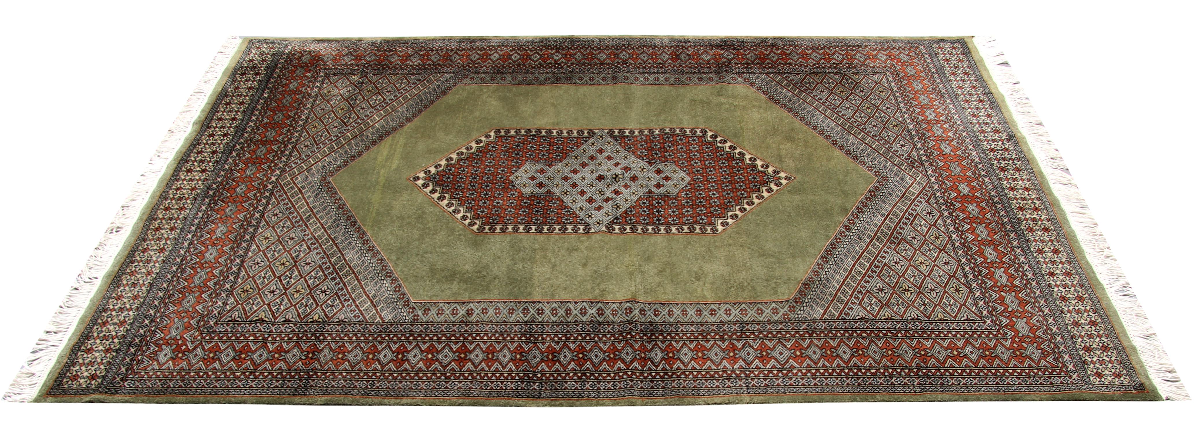 This grand area rug was woven in the 1980s with a bold central medallion woven with floral and geometric motifs, in accents of red and ivory on a green background. This has then been framed by a layered highly decorative border woven with the same