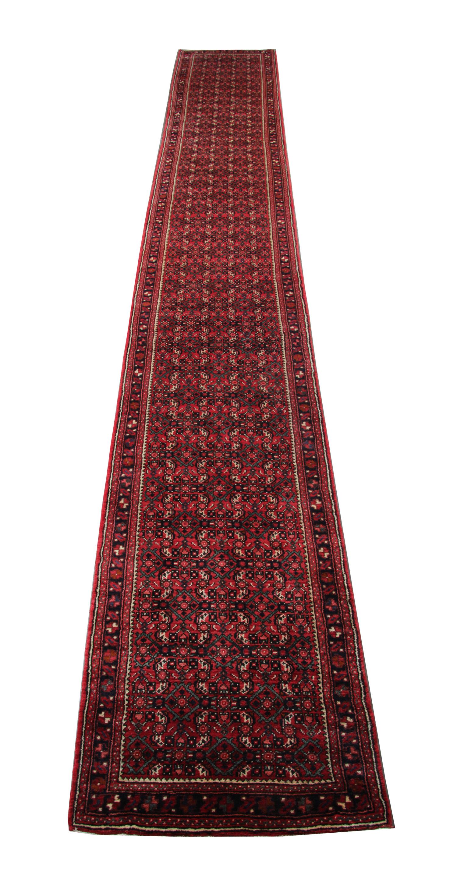 This elegant hand made wool runner rug was constructed in 1960. The fine central design features a rich red background with brown, cream and black accents that make up the sophisticated repeat geometric pattern. Woven with elegance, this piece is