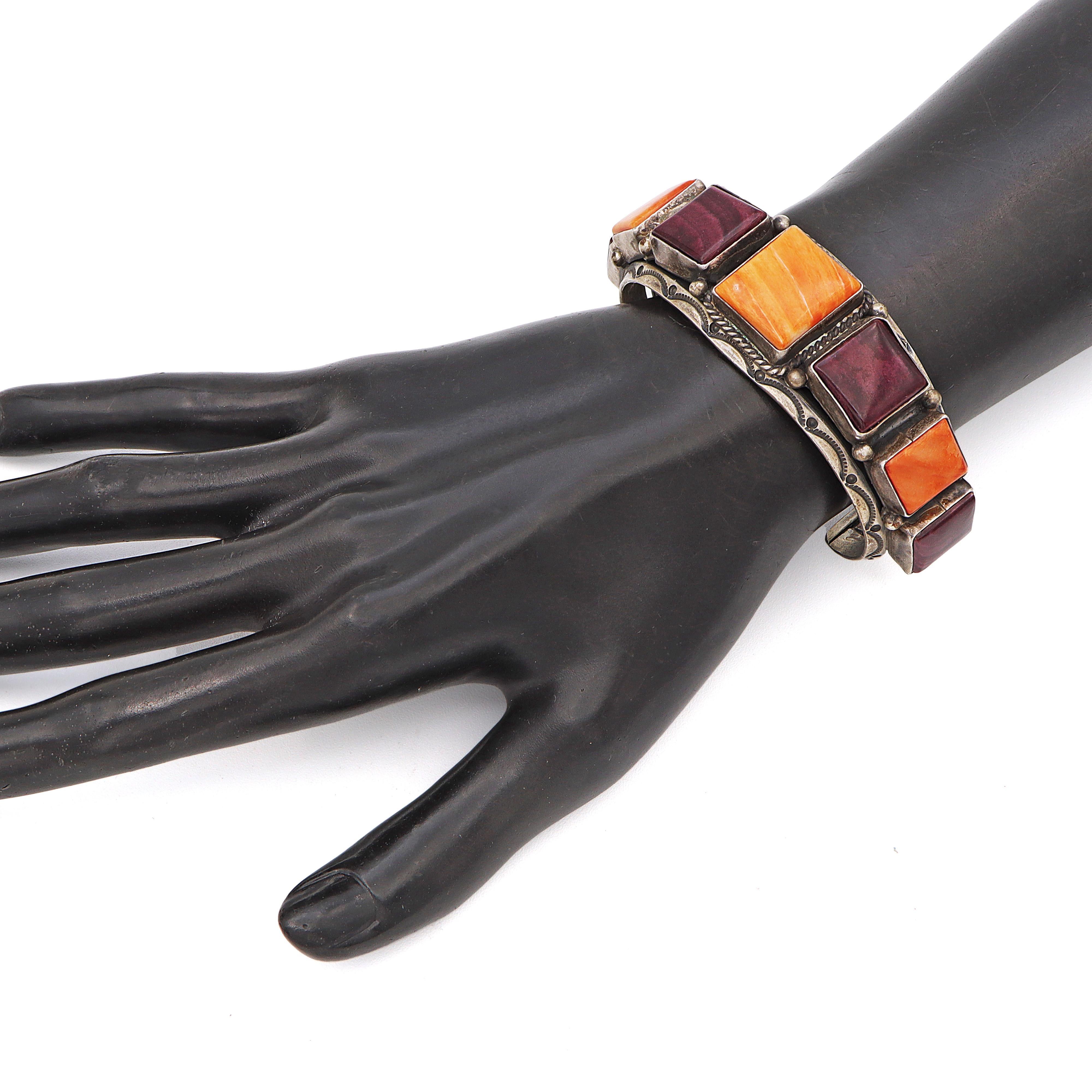 This striking cuff bracelet by Running Bear is a stunning showcase of traditional Navajo artistry. Crafted from sterling silver, it features a bold row of square and rectangular cabochons in vivid shades of orange and deep purple—likely spiny oyster
