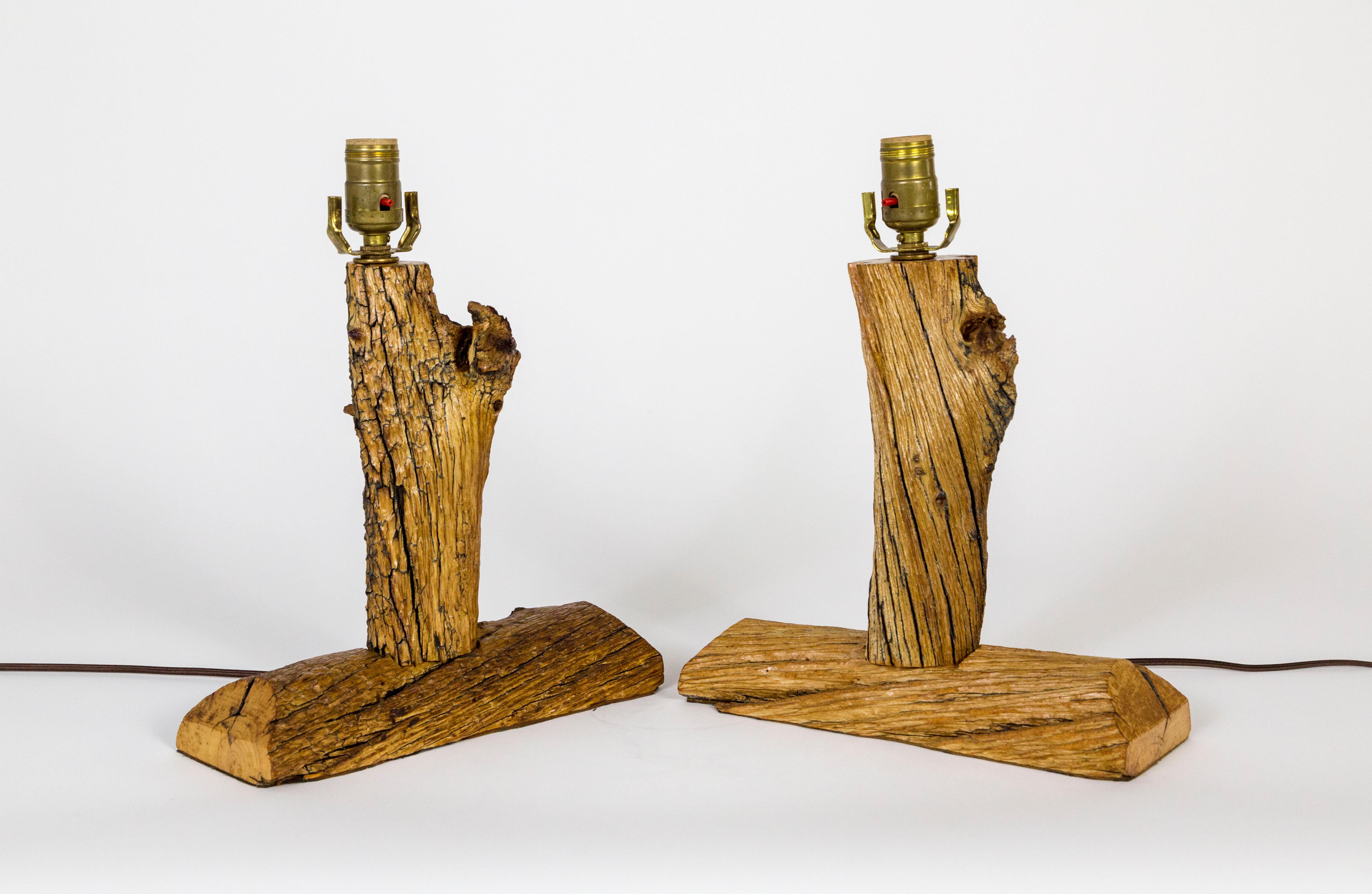 A pair of handmade, log table lamps created in the mid 20th century. The wood shape and texture is particularly interesting with its gnarls, rich color, and diagonal cracks. A nice finish; sealed. The original sockets have charming, red tipped, push