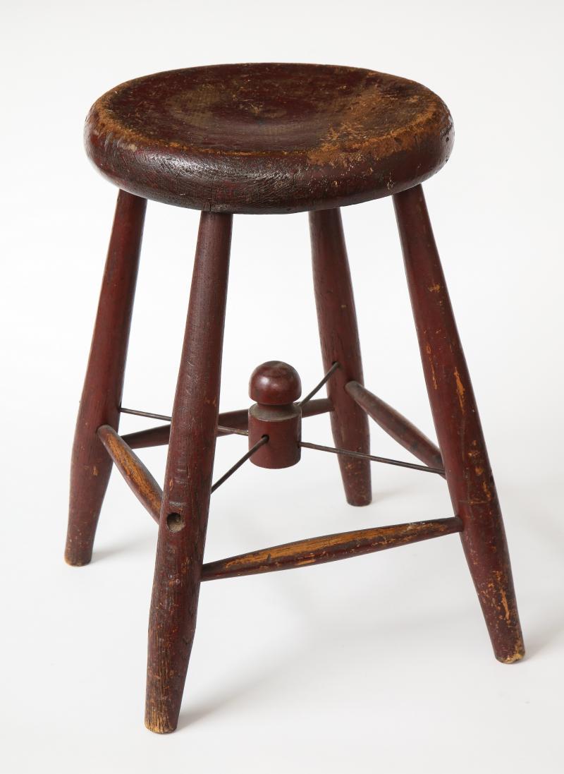 Rustikaler vierbeiniger kastanienbrauner Holzhocker im Vintage-Stil. Die Querstreben aus Metall treffen sich an einem hübschen Mittelstück, das auf der Sitzfläche eine charmante Patina aufweist.

