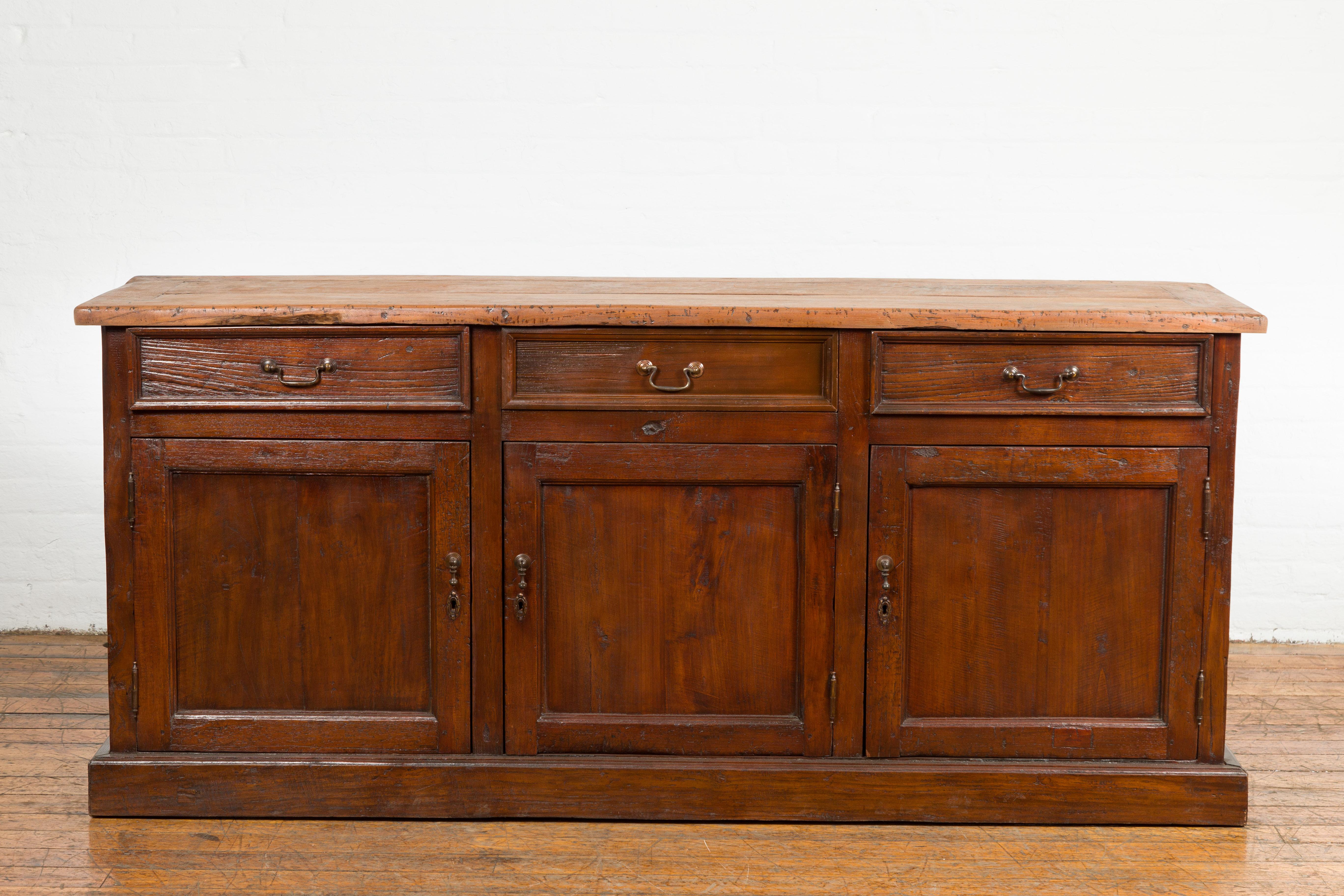 A vintage Indonesian wooden buffet from the mid 20th century with three drawers over three doors. Presenting a fusion of functionality and classic Indonesian aesthetics, this vintage wooden buffet from the mid-20th century features a pragmatic