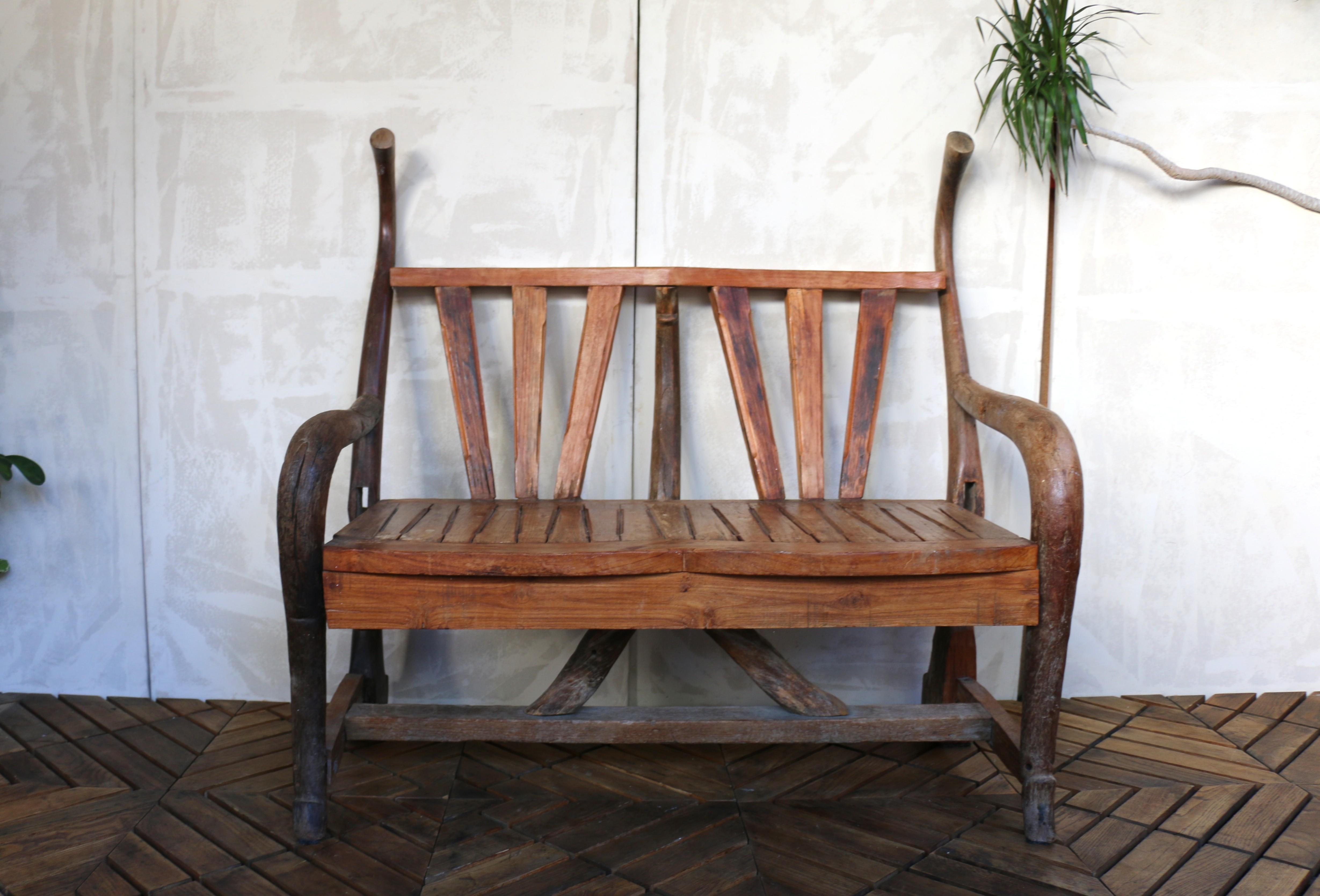 Un banc d'extérieur rustique vintage fabriqué en bois présente une assise et un dossier à lattes, ainsi que des accoudoirs incurvés qui s'étendent depuis les pieds avant. Ce banc esthétique en bois massif est idéal pour les patios, les jardins, les