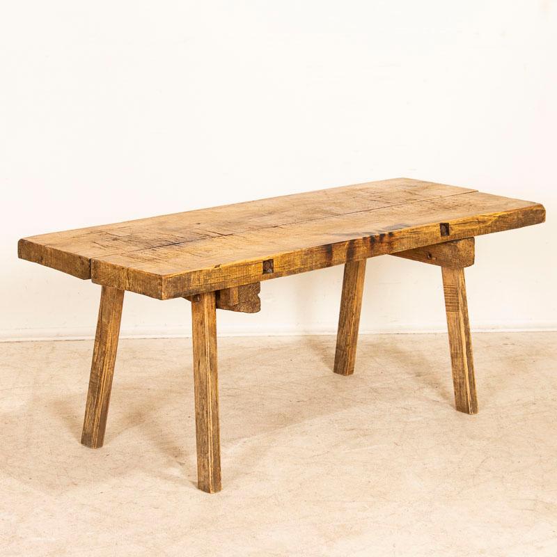 The thick slab top draws one to this rustic coffee table due to the heavy distress seen in every scratch, crack, burn mark and gouge that came from years of constant use (likely in a butcher's shop). There is typical age-related separation of the 2