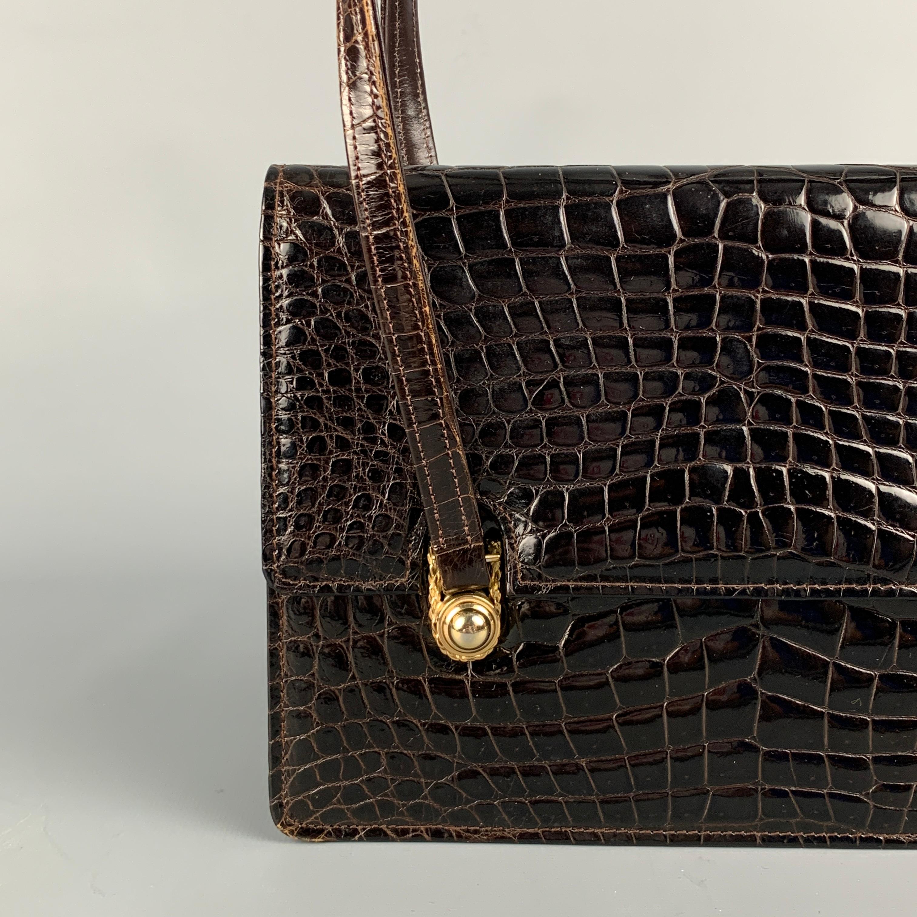Vintage SACHA handbag comes in a brown textured alligator leather featuring double top handles, gold tone hardware, inner compartments, and a snap button closure. 

Very Good Pre-Owned Condition.

Measurements:

Length: 9 in.
Width: 3 in.
Height: