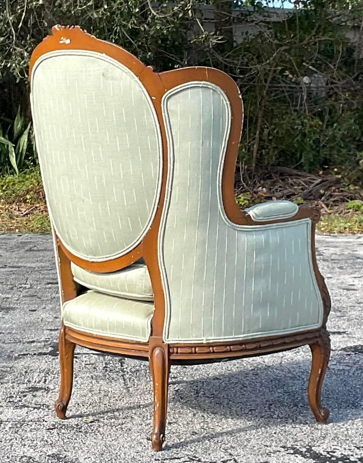 A stunning vintage wingback chair in a lovely sage green with a carefully carved wooden trim. Acquired at a Palm Beach estate.