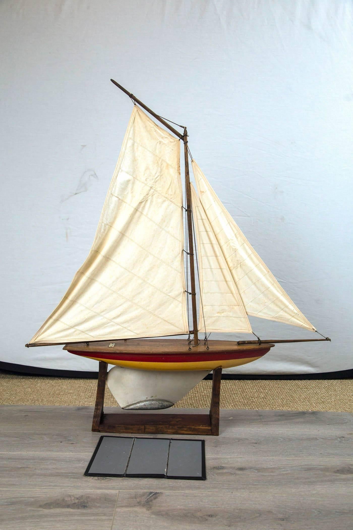 Vintage sailing pond boat, 'yacht Ailsa, circa 1930, Scotland. Handmade craftsmanship with yellow and red painted hull, varnished wood deck, metal rudder. Plaque reads 'Ailsa yacht, made in larges, Scotland'. Custom oak stand.