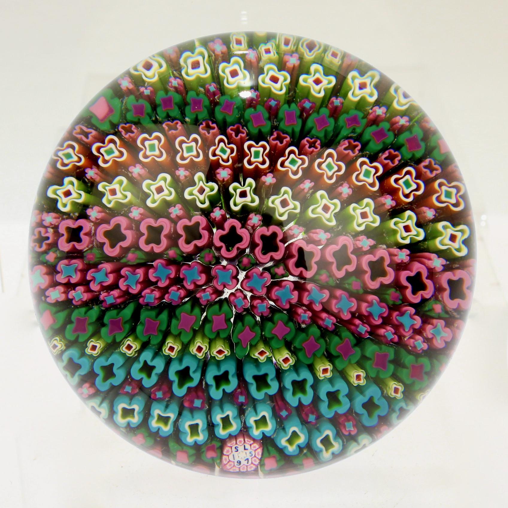 Un très beau presse-papiers en verre d'art hawaïen Millefiori de Saint Louis. 

Il comporte de multiples rangées de millefiori colorés qui créent un tapis de sol de facto dans des tons principalement verts. 

Il a une canne signature SL 1975 pour