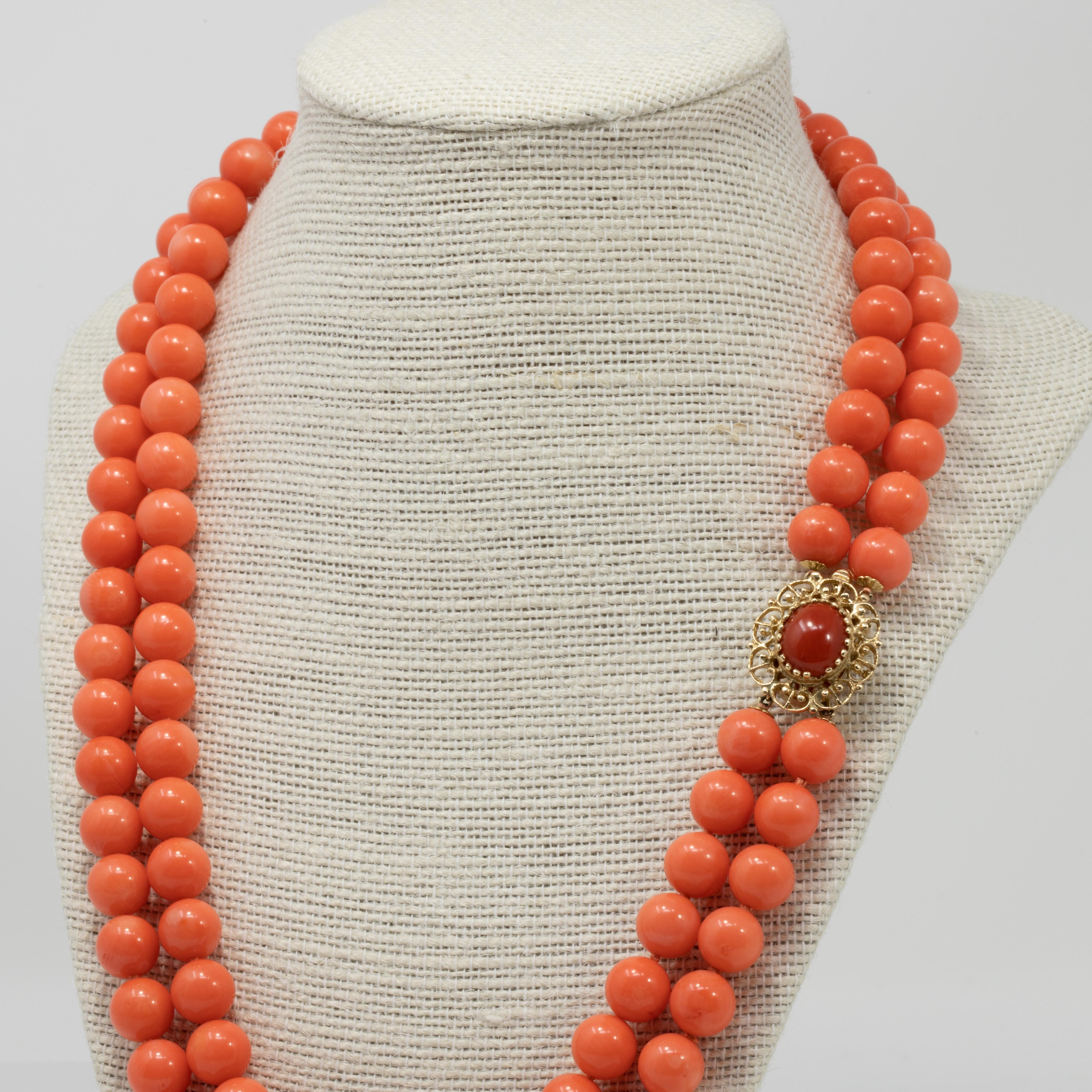 An elegant vintage salmon coral bead necklace. Features two strands of coral beads, fastened with a luxurious 14K yellow gold clasp, with a coral cabochon prong-set in the center.

Coral beads are 9.75mm in diameter.

A single small prong on the