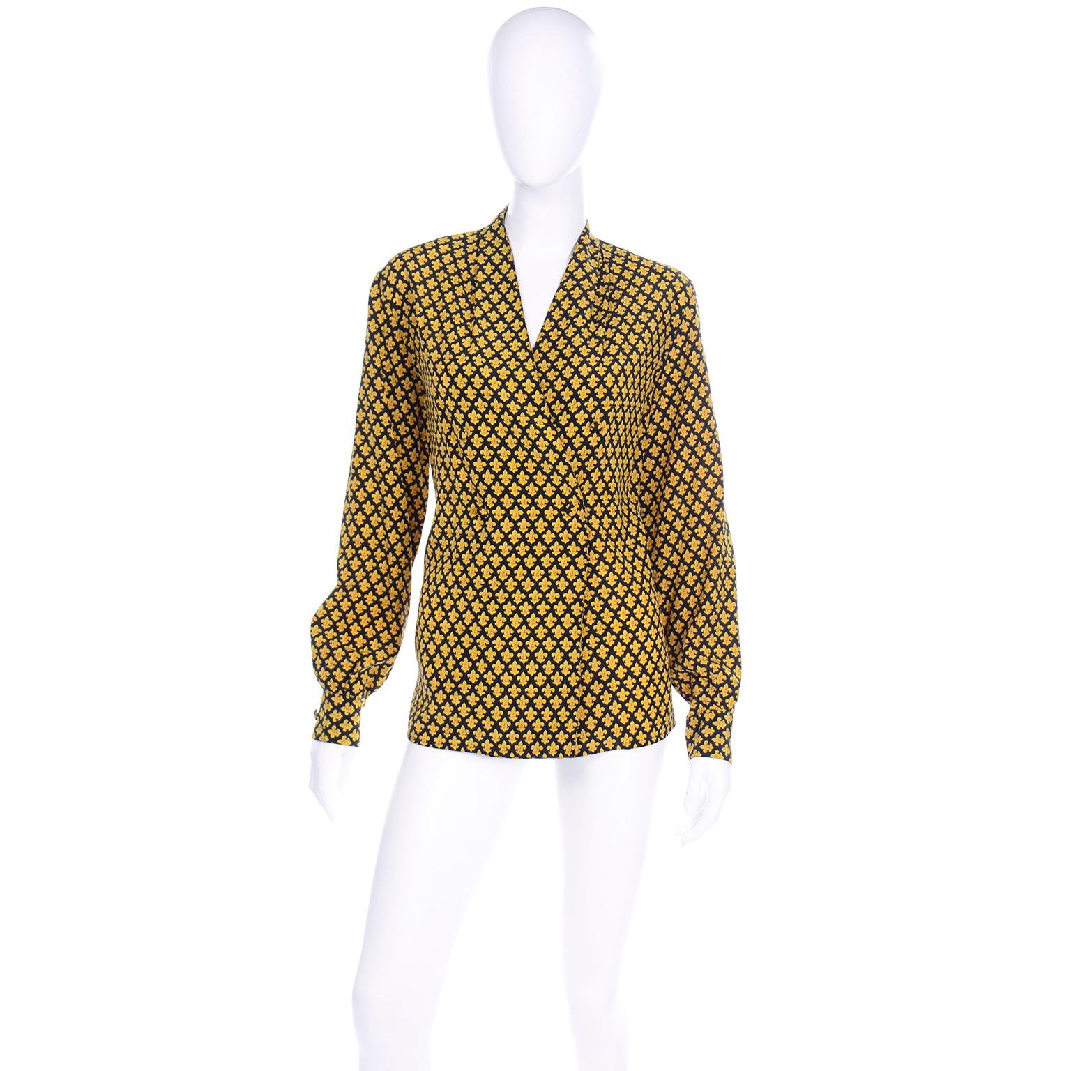 This vintage Salvatore Ferragamo long sleeve silk blouse is in a lovely fleur de lis black and gold print. This double breasted blouse is collarless and has a pleated detail near the collar that makes this drape so effortlessly. The fabric covered
