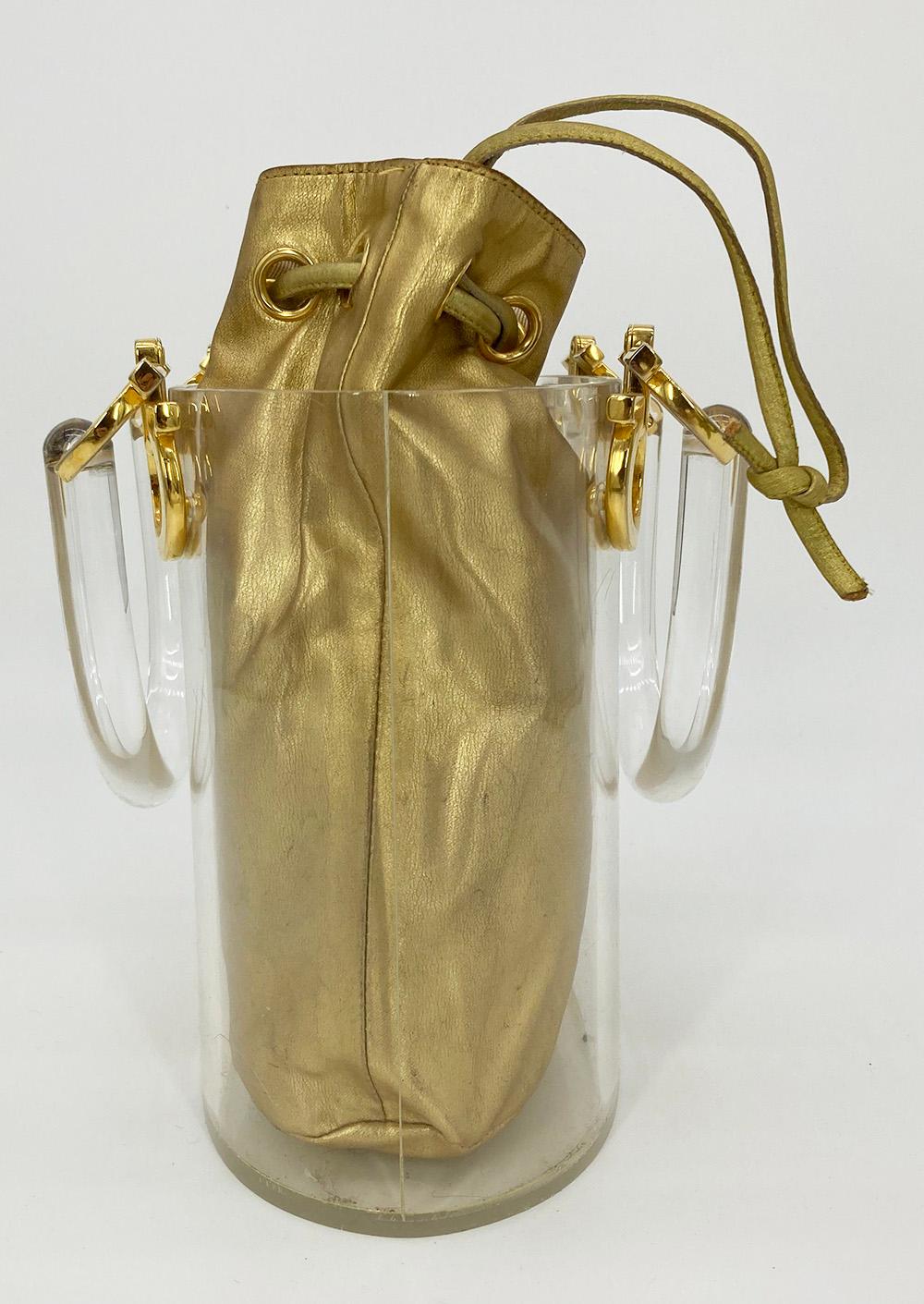 Vintage Salvatore Ferragamo Clear Bucket Bag with Gold Pouch in fair condition. Clear acrylic curved hardshell bucket with double handles and gold tone signature ferragamo hardware at each end of handles. Gold leather drawstring interior pouch can