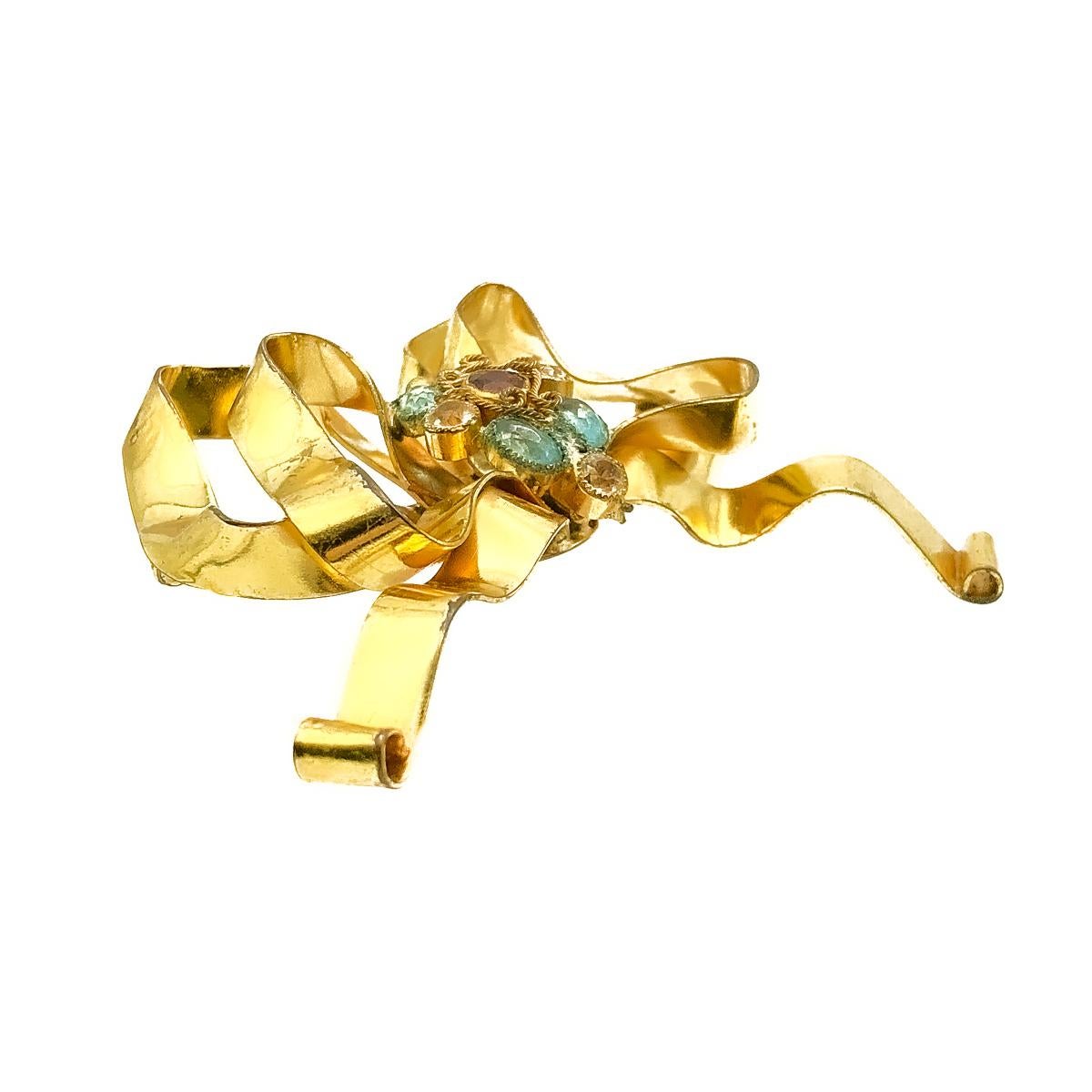 Vintage Sandor Bow Brooch. Crafted in gold plated metal with coloured glass paste stones. Featuring a large floppy bow design finished with a central display of aqua, garnet and white coloured stones. The metalwork around the stones inspired by