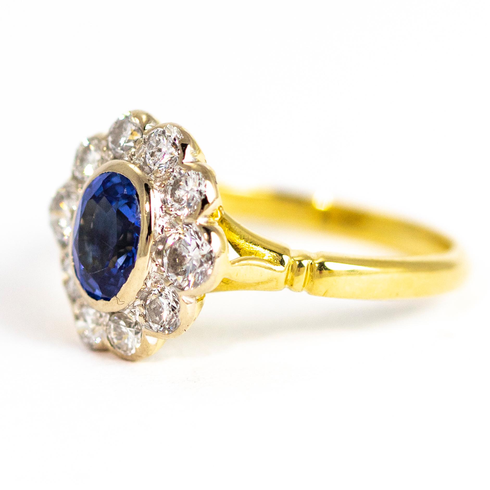 A large oval medium hue blue sapphire sits at the centre of a hoop of bright, clean old European cut diamonds which measure approximately a total of 1carat. The back of the setting is modelled into a sweet flower motif and all is made of 18ct