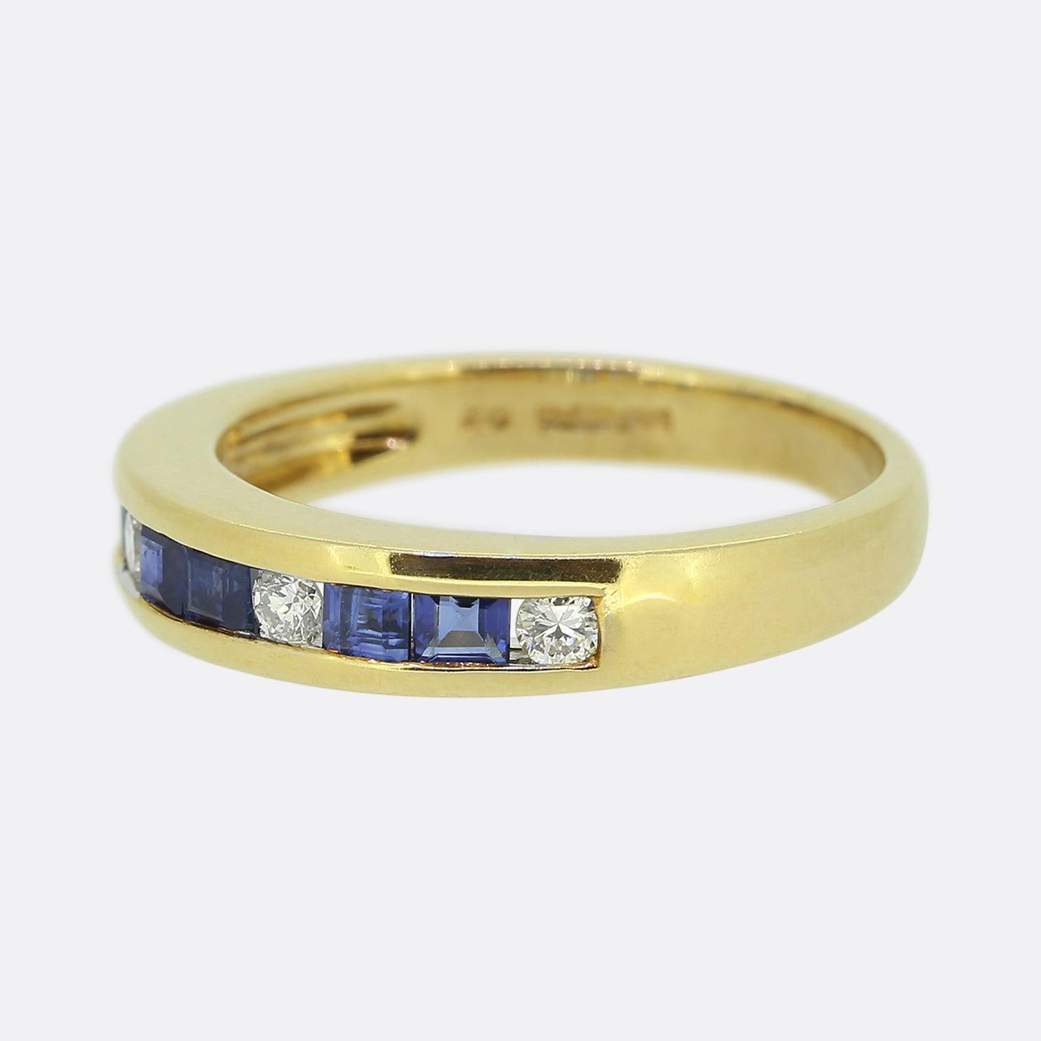 Here we have a classically styled sapphire and diamond band ring. An 18ct yellow gold mount plays host to an alternating array of paired square calibrated sapphires and single round brilliant cut diamonds. All stones have been neatly rub-over set in