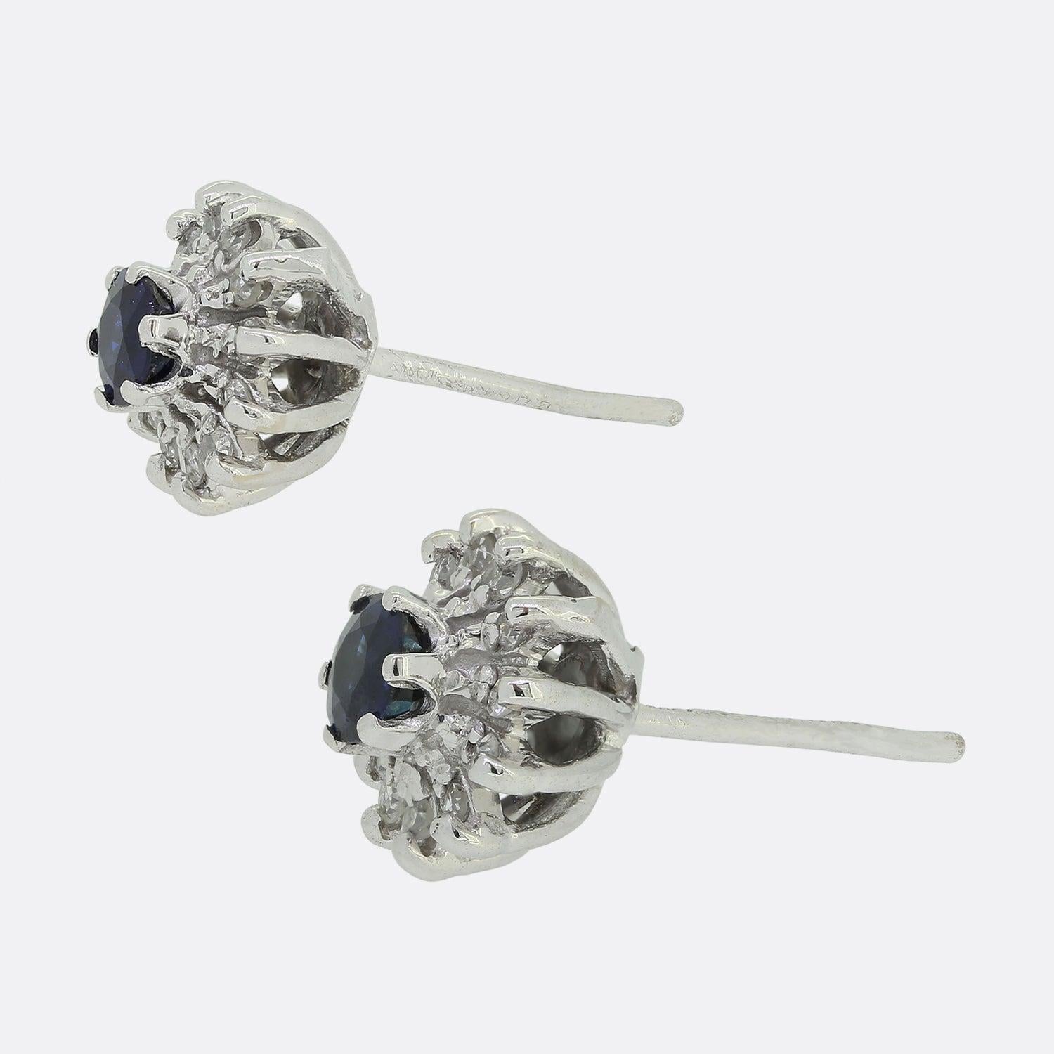Here we have vintage pair of 18ct sapphire and diamond earrings. Each white gold mount plays host to a centralised, slightly risen round sapphire possessing a rich deep blue iridescent hue. This principle stone is then surrounded by an array of