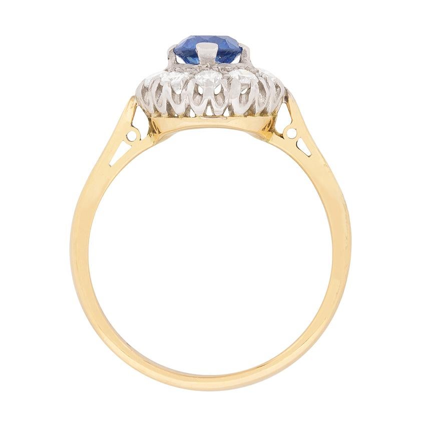 This colourful c.1950s take on a classic cluster design centres a bright blue sapphire within a grain-set halo of 0.50ct round brilliant cut diamonds.

In classic two-tone vintage style, the stones are mounted in platinum, with the balance of the