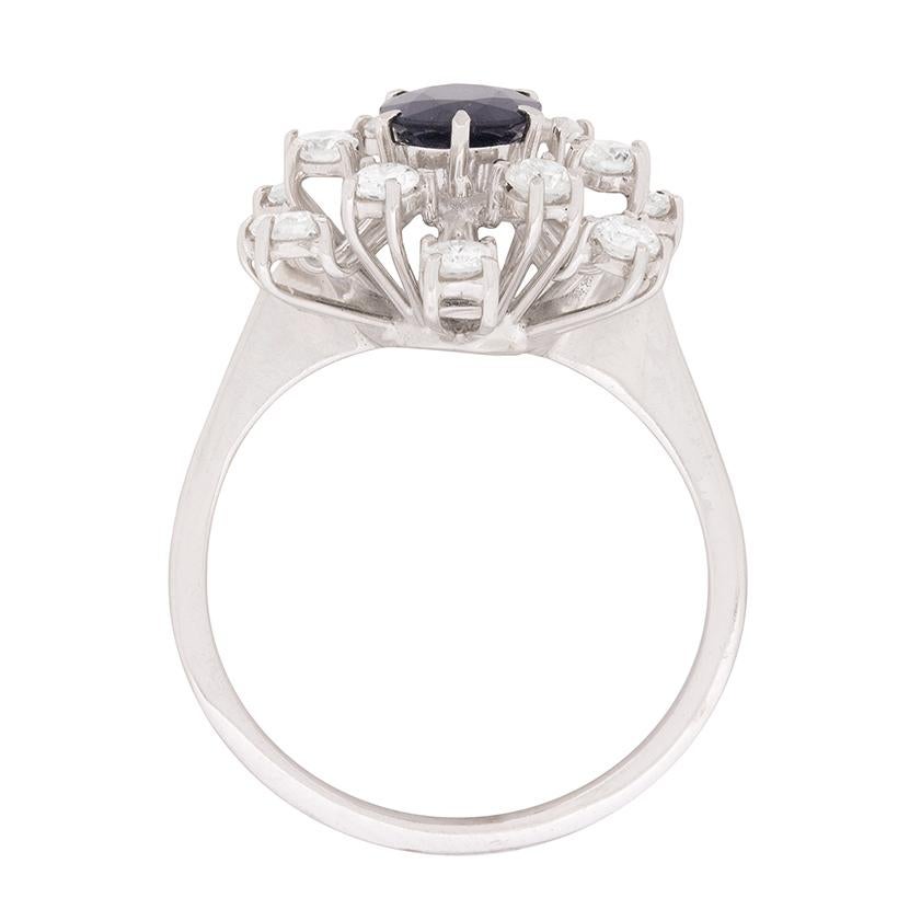 A starburst of 0.60ct round brilliant cut diamonds radiates from the dark blue, oval-shaped sapphire at the centre of this disco era cluster ring.

Crafted entirely in 18 carat white gold, the ring’s original wirework setting is a classic example of
