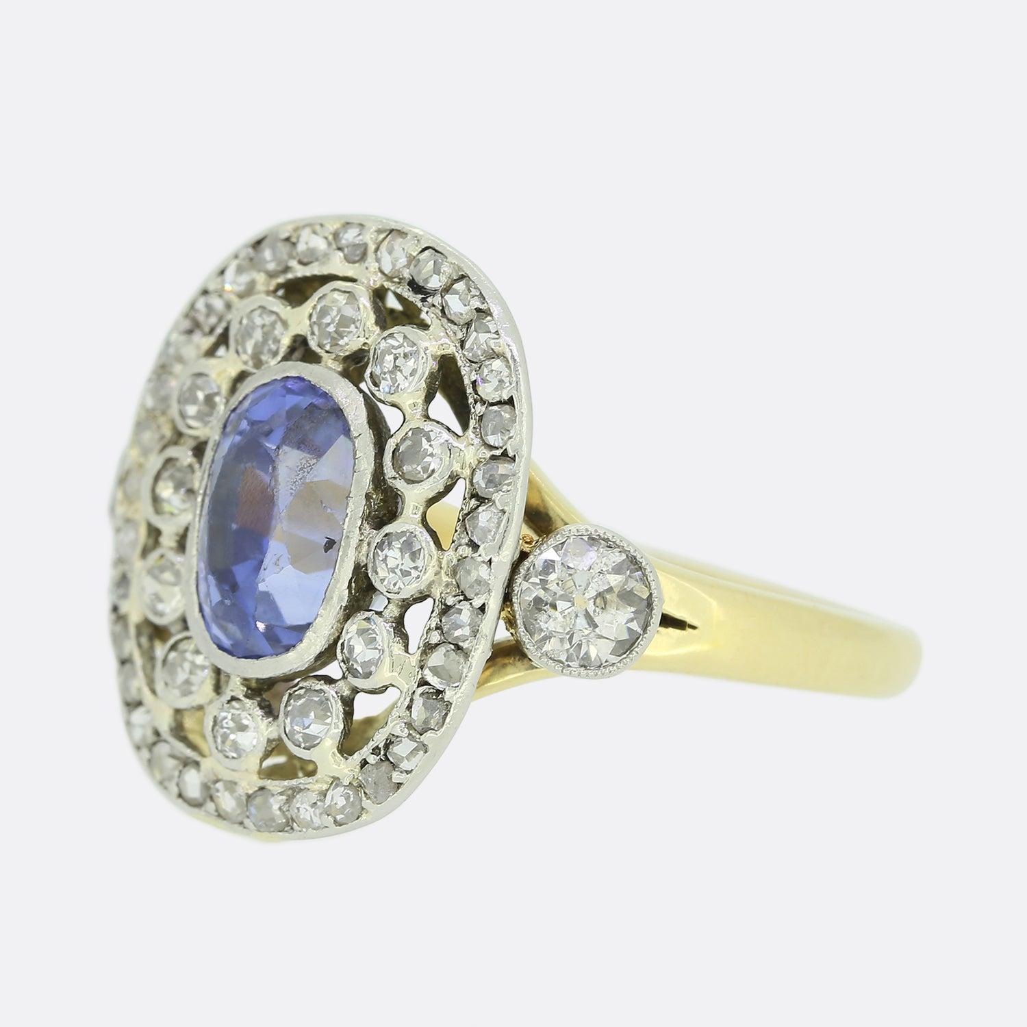 This is a marvellous 18ct yellow gold ring focally featuring a single oval shaped sapphire at the centre of the face believed to be of Ceylon origin. The ring's open, multi-layered structure presents firstly, a cluster of old cut diamonds and then a