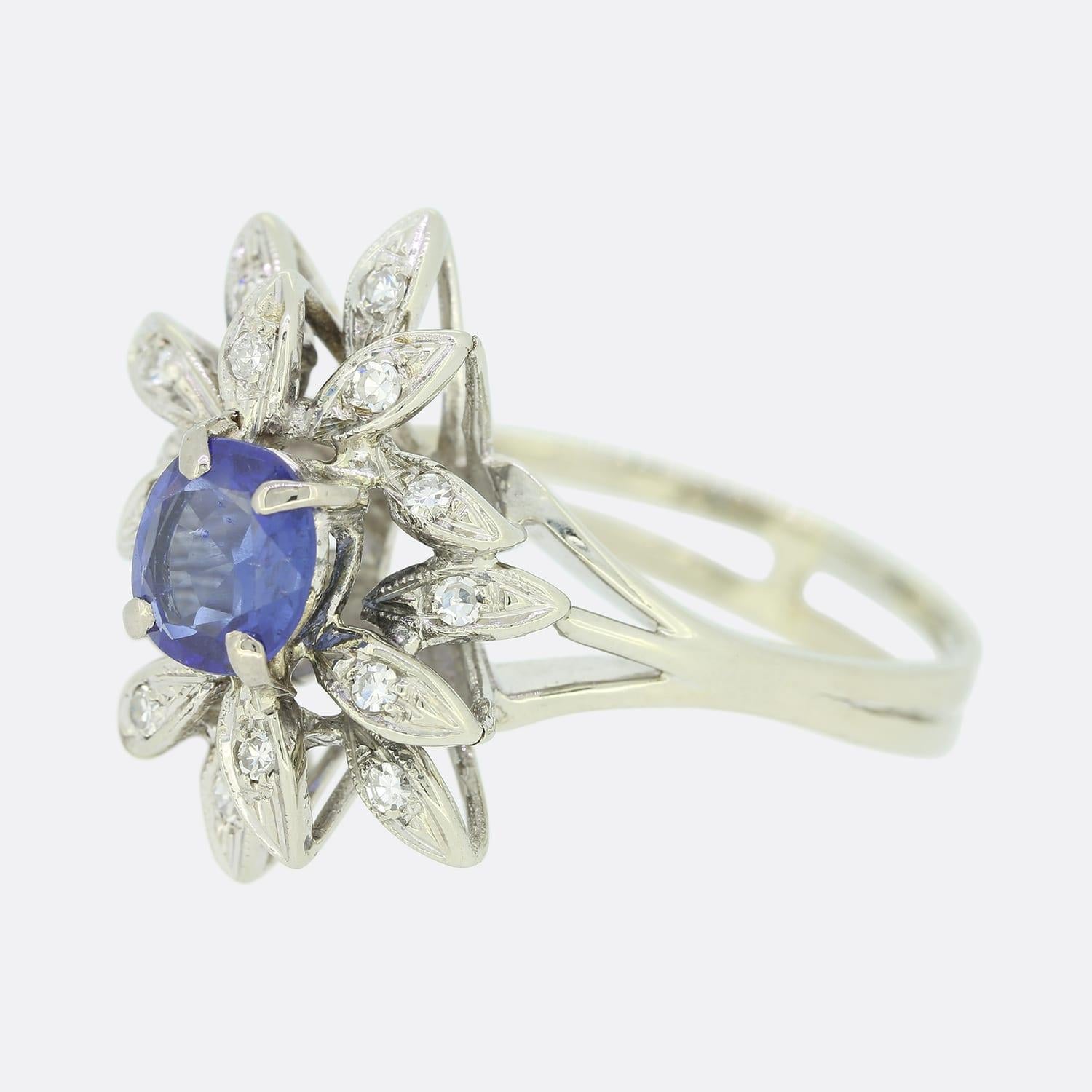 This is a beautiful vintage sapphire and diamond cluster ring. The ring features a central cushion cut sapphire surrounded by multiple single cut diamonds in an abstract setting. The sapphire is a royal blue hue and raised in a four claw