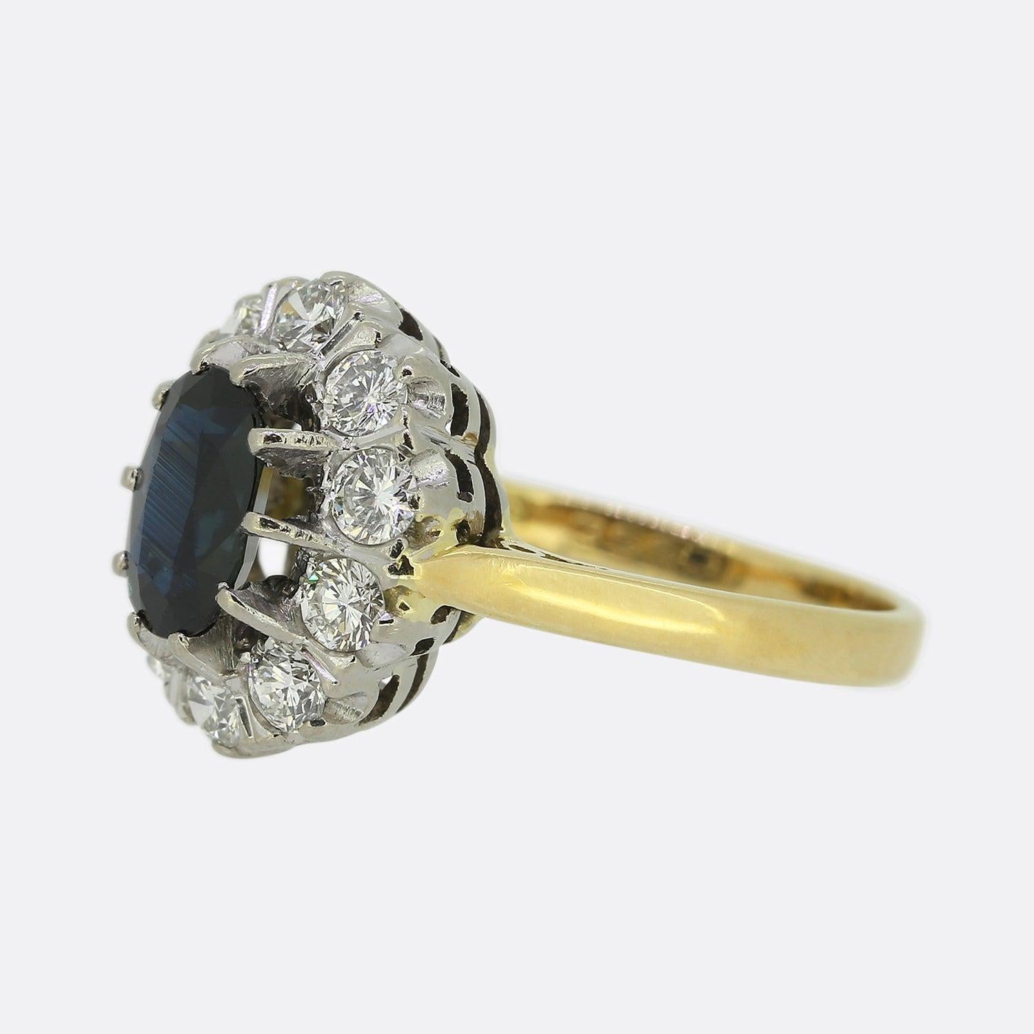 Here we have an 18ct yellow gold sapphire and diamond cluster ring. An oval shaped sapphire possessing a deep dark navy tone sits in a 10 clawed setting at the centre of the piece. This principle stone is then circulated and accentuated by a frame