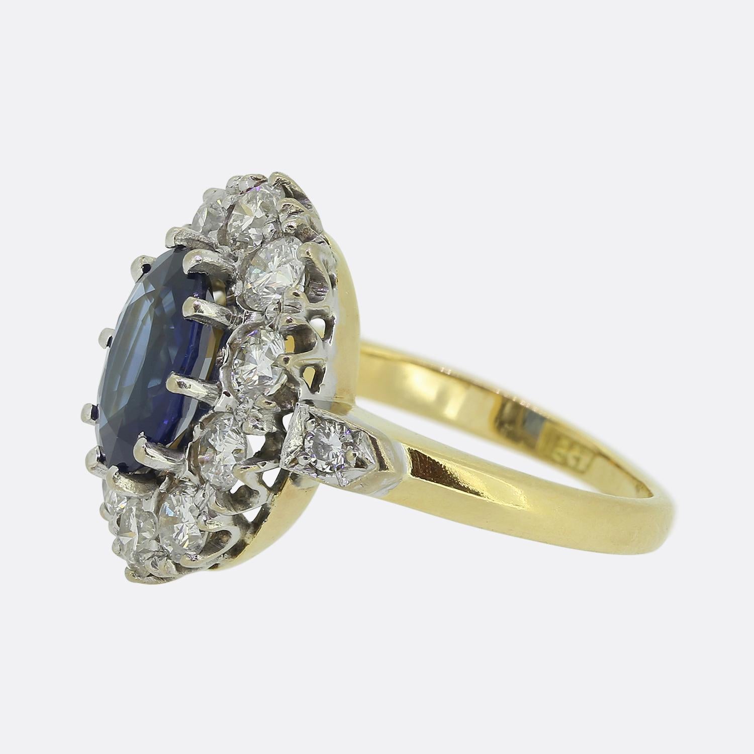 Here we have a stunning sapphire and diamond cluster ring. This vintage ring features a mid to dark blue sapphire that is surrounded by ten round brilliant cut diamonds. It is crafted in 18ct yellow gold with white gold settings for the diamonds and