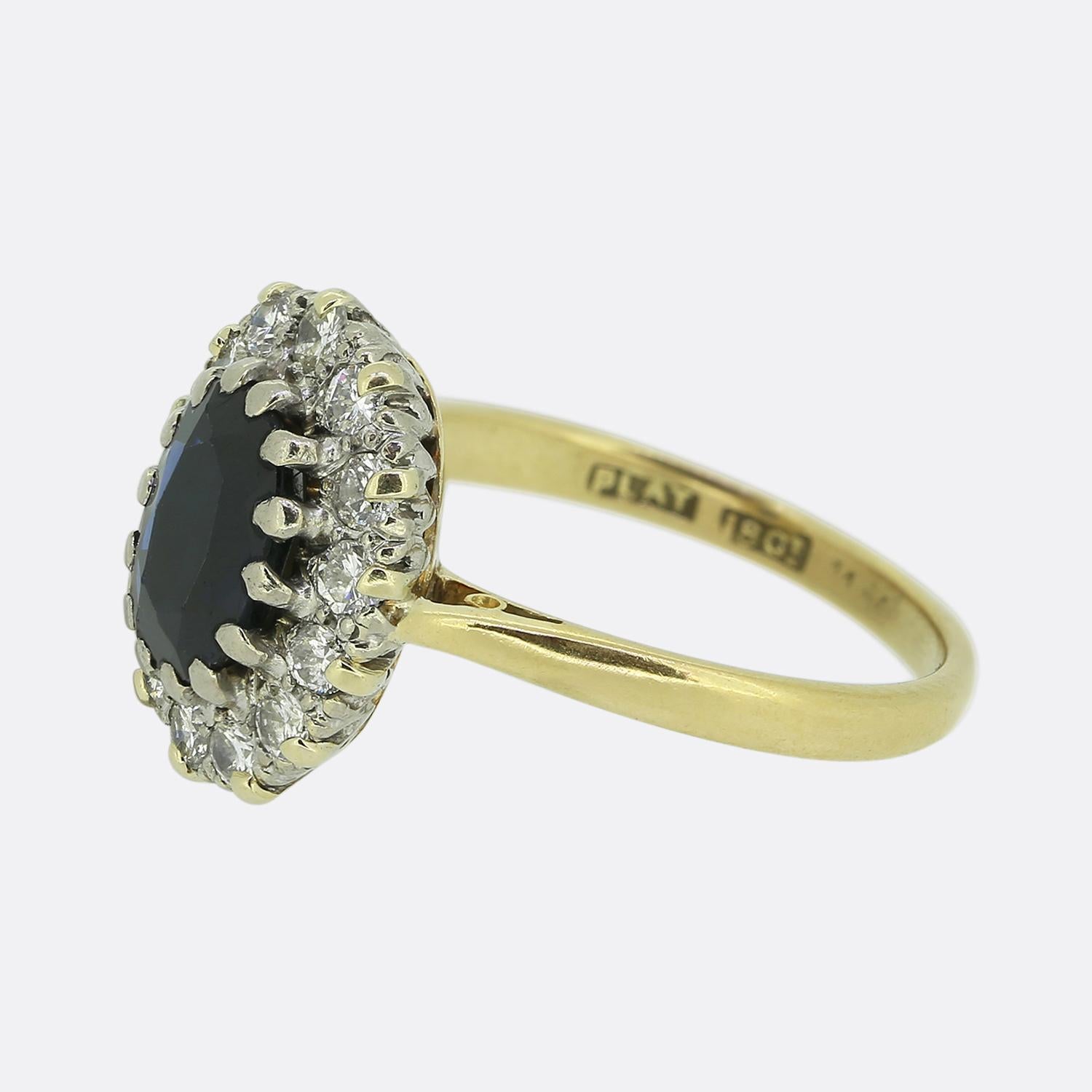 Here we have a classic sapphire and diamond cluster ring. This vintage ring features a mid to dark blue sapphire that is surrounded by fourteen round brilliant cut diamonds. It is crafted in 18ct yellow gold with platinum settings for the diamonds