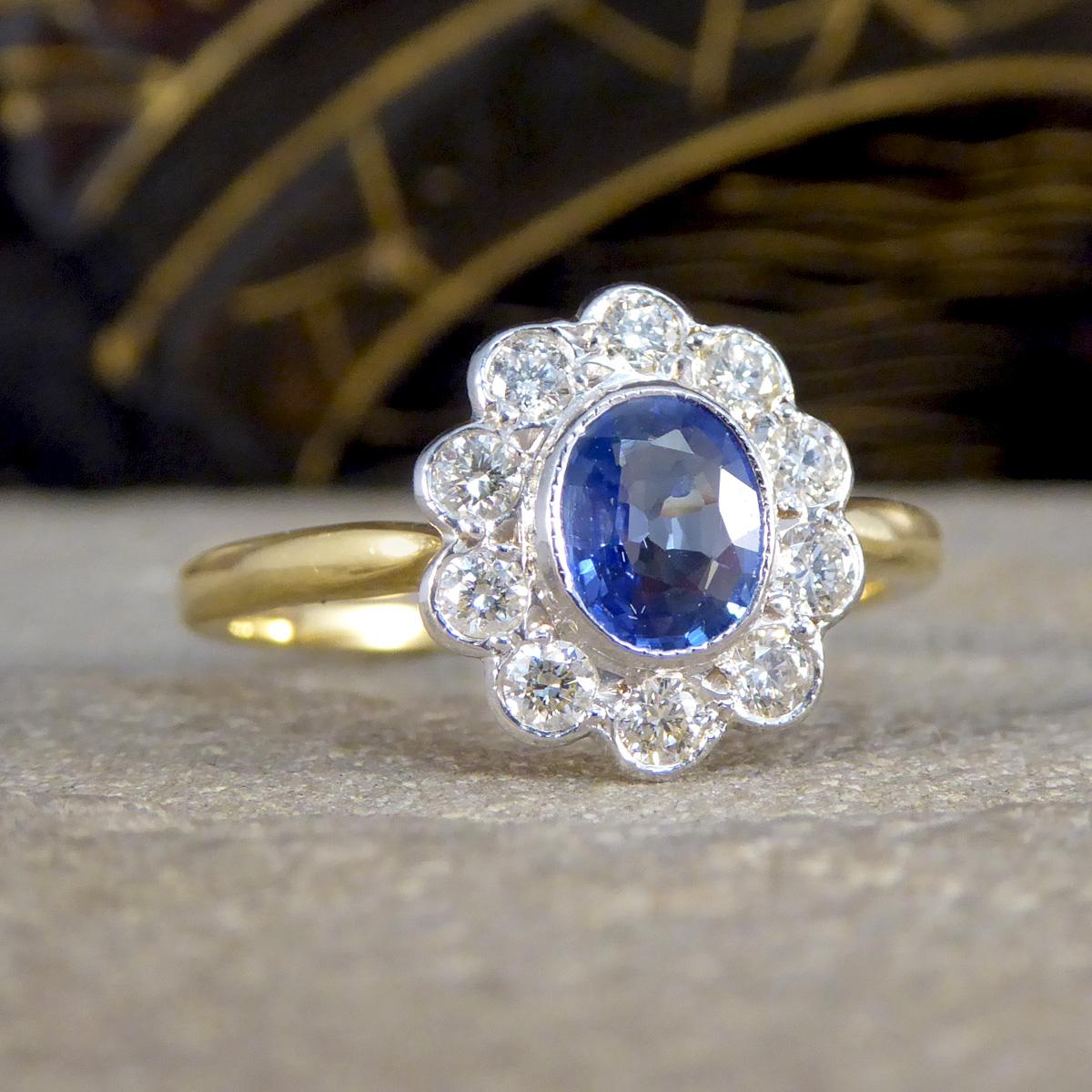 Experience the allure of bygone elegance with this vintage Sapphire and Diamond cluster ring. This exquisite piece features a central 0.70ct bezel-set sapphire, with a light and enchanting blue tone, which is gracefully complemented by a cluster of