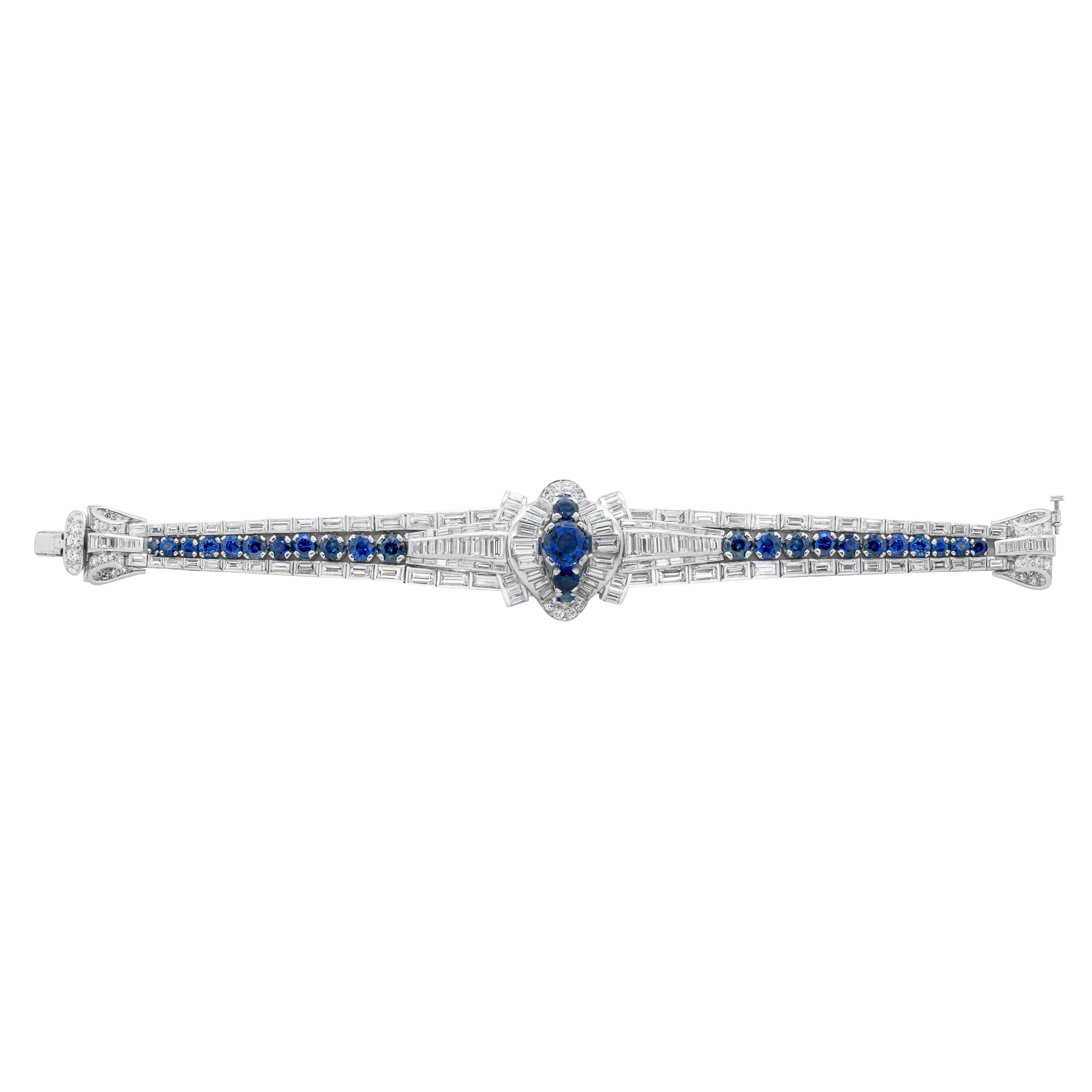 Dating back to the 1950's, this magnificent handmade bracelet features a large royal blue sapphire in the centre, weighing approximately 3.10 carats, set in-between two smaller sapphires inside a halo of channel set diamonds. The bracelet is further