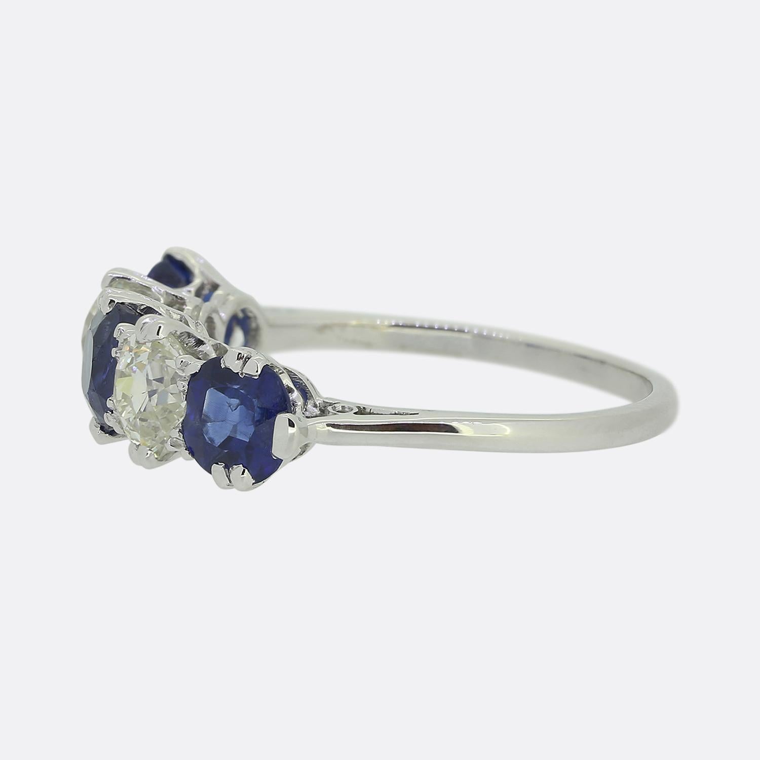 Here we have a classically styled five-stone ring. This vintage piece has been crafted from platinum and showcases an alternating array of sapphires and diamonds in a slight concave single line formation. A trio of excellently matched, cornflower