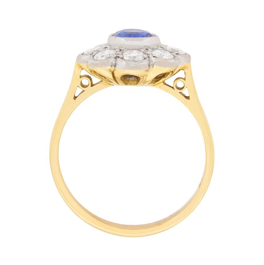 A bright blue natural 0.50ct sapphire in an 18 carat white gold rubover mounting is the centre to eight 0.10ct round brilliant cut diamond ‘petals’ totalling to 0.80ct in this millegrained 1970s rendition of the always fashionable sapphire and