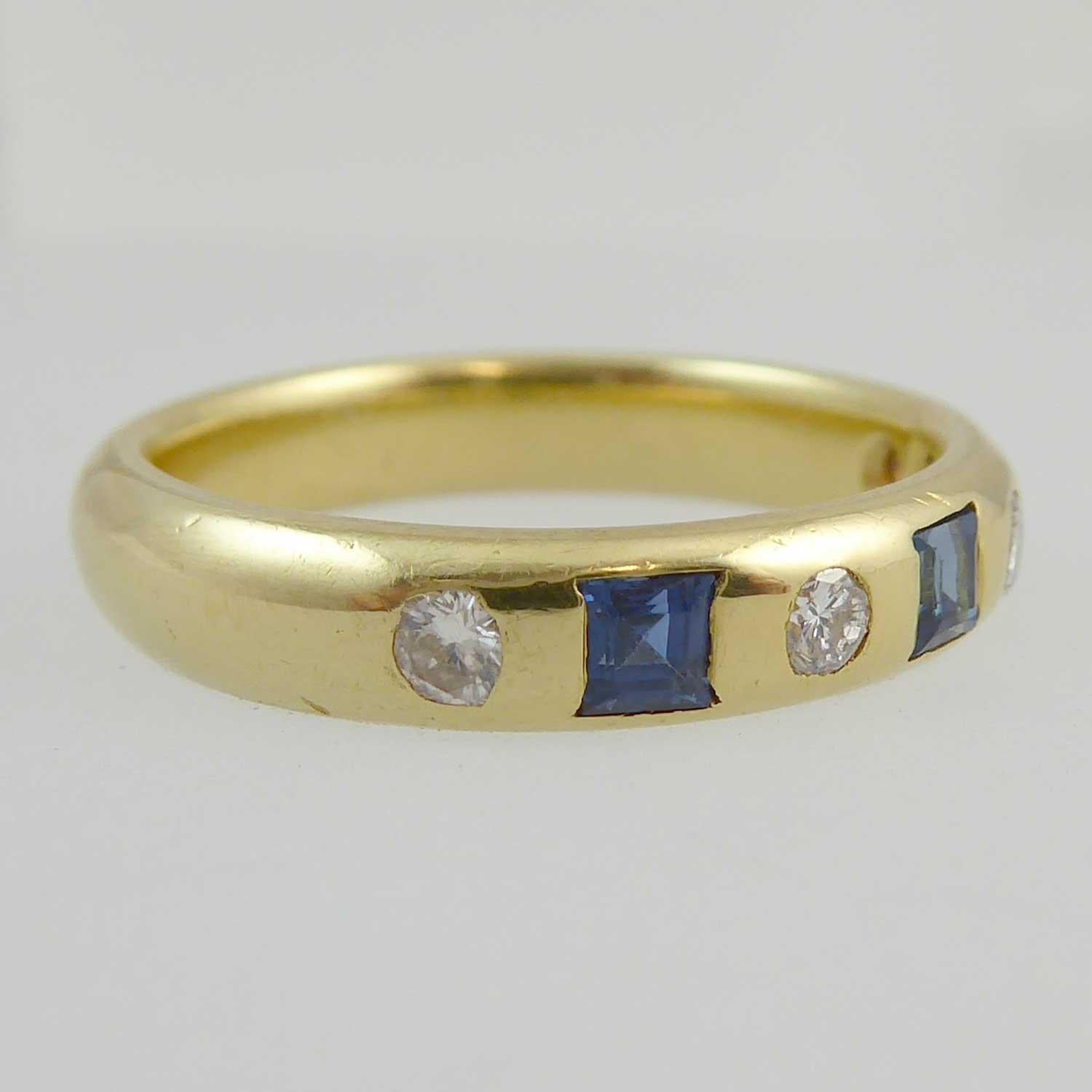 A pre-owned sapphire and diamond set dress ring featuring three trap cut sapphires alternating with four round brilliant cut diamonds in a channel setting across the finger.  The sapphires measure an approxiimate average of 2.5mm square and have a