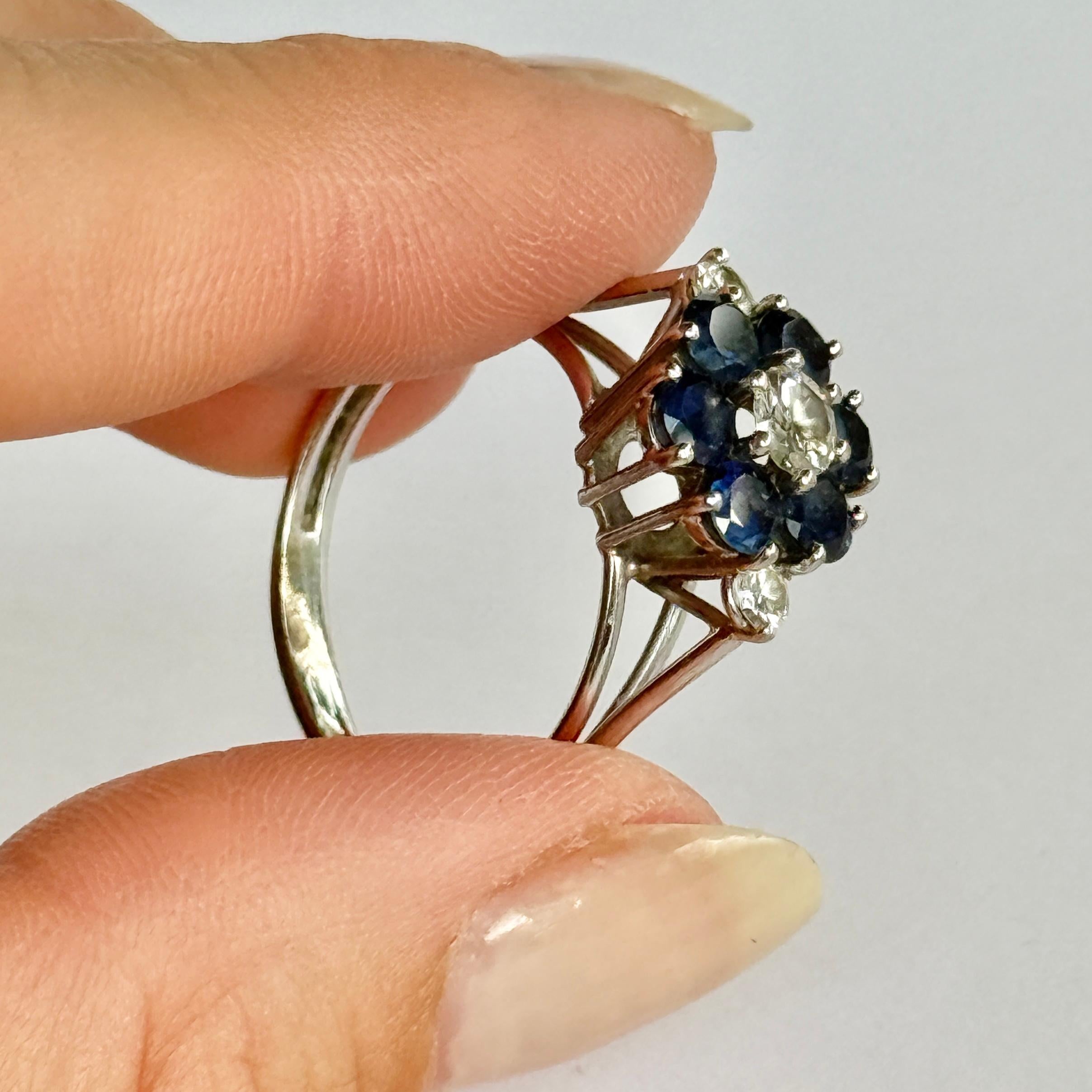 This striking sapphire and diamond cluster ring is modelled in platinum. The sapphires measure 20pts each and the diamond at the centre measures 35pts. The shoulders hold a 10pt diamond on each.

Ring Size: R 1/2 or 8 3/4 
Cluster Diameter: