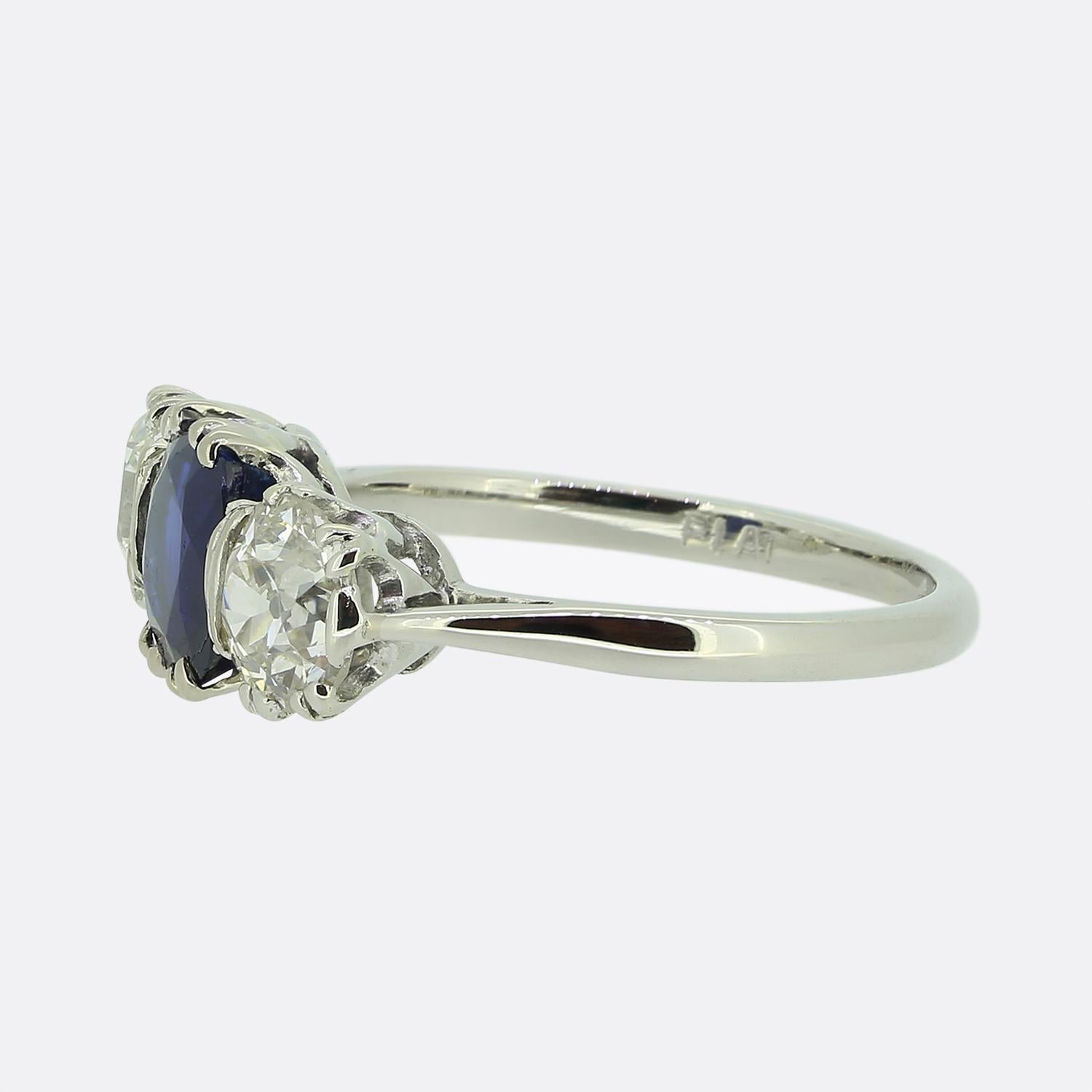 Ecco un anello a tre pietre dallo stile classico. Questo pezzo vintage è stato realizzato in platino e presenta uno zaffiro rotondo a forma di cuscino al centro del quadrante. Questa pietra principale possiede una tonalità di colore navy profondo,