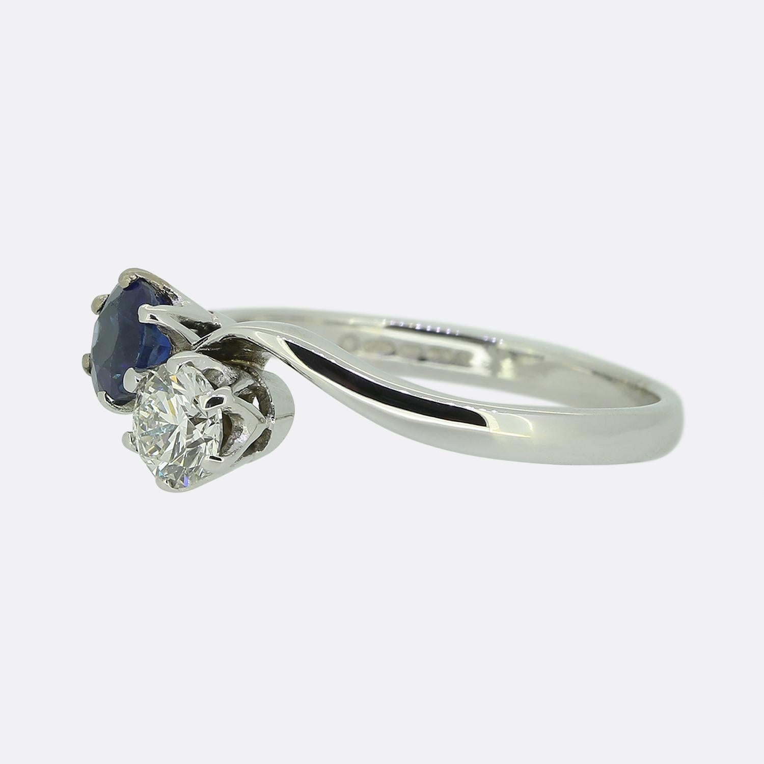 Here we have a lovely two-stone twist ring. This vintage piece has been crafted from 18ct white gold and showcases single bright white round brilliant cut diamond alongside a round faceted sapphire possessing a playful navy blue tone. Both stones