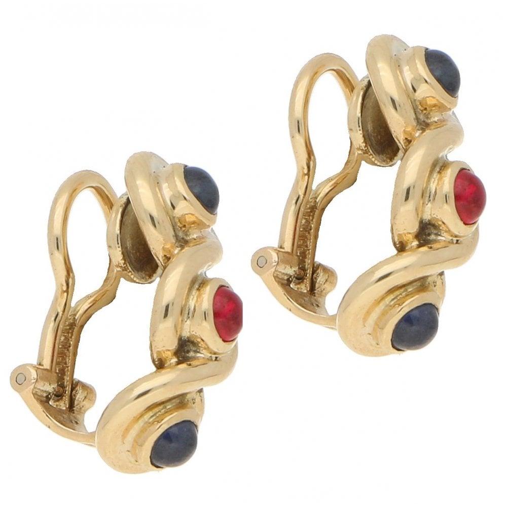 A pair of sapphire and ruby infinity clip earrings in 18-karat yellow gold, circa 1982. 
Each earring is designed as a triple infinity, bezel set with a ruby cabochon at the centre and a sapphire cabochon at each end. 
The earrings are secured with