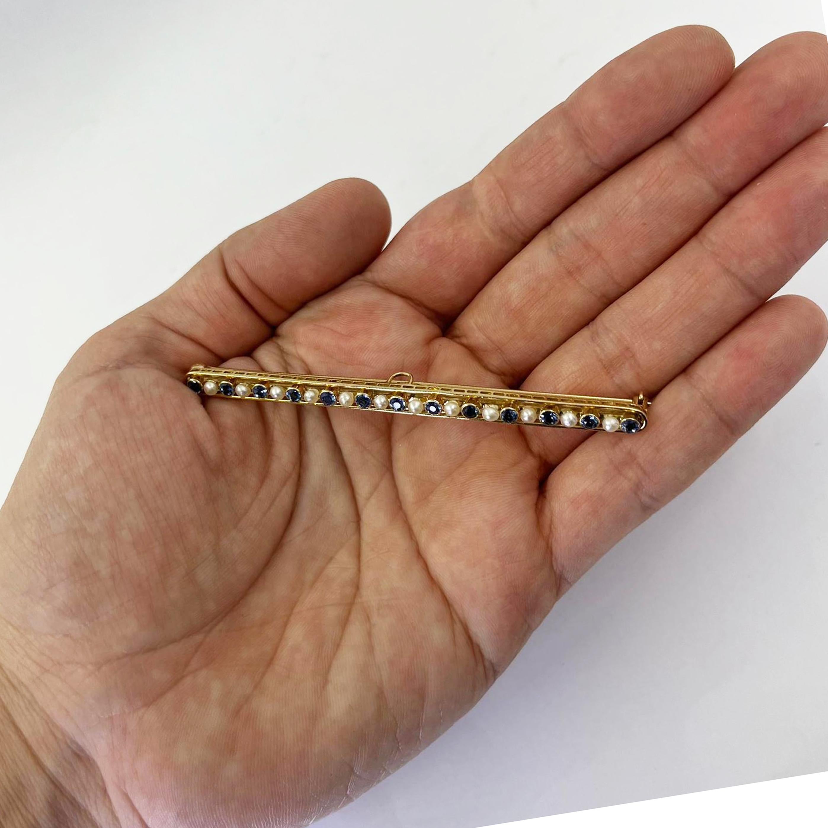 14 karat yellow gold narrow bar pin featuring 13 bezel-set round cornflower blue sapphires totaling 0.65 carats accented by 12 seed pearls. 3 inches long with pin and locking catch at back. Finished weight is 6.0 grams.
