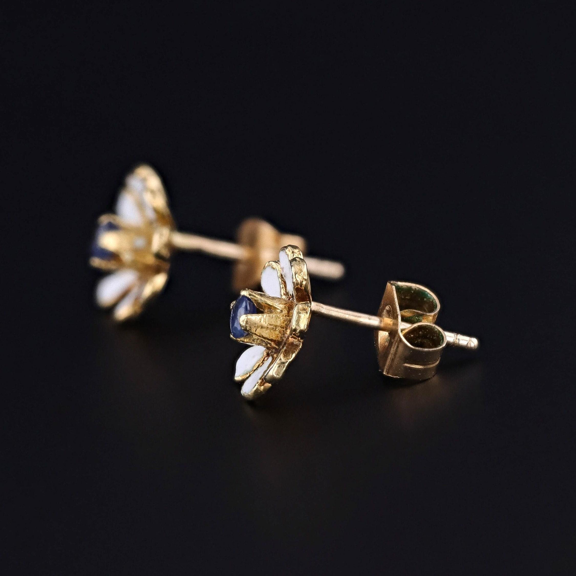 Diese Vintage-Ohrringe (ca. 1940-1950) zeigen Gänseblümchen aus 14-karätigem Gold mit weißer Emaille und blauen Saphiren.

Jeder Ohrring misst 0,35 Zoll breit, und sie sind in gutem Zustand.

MATERIAL:  14k Gold; Emaille; Saphir
