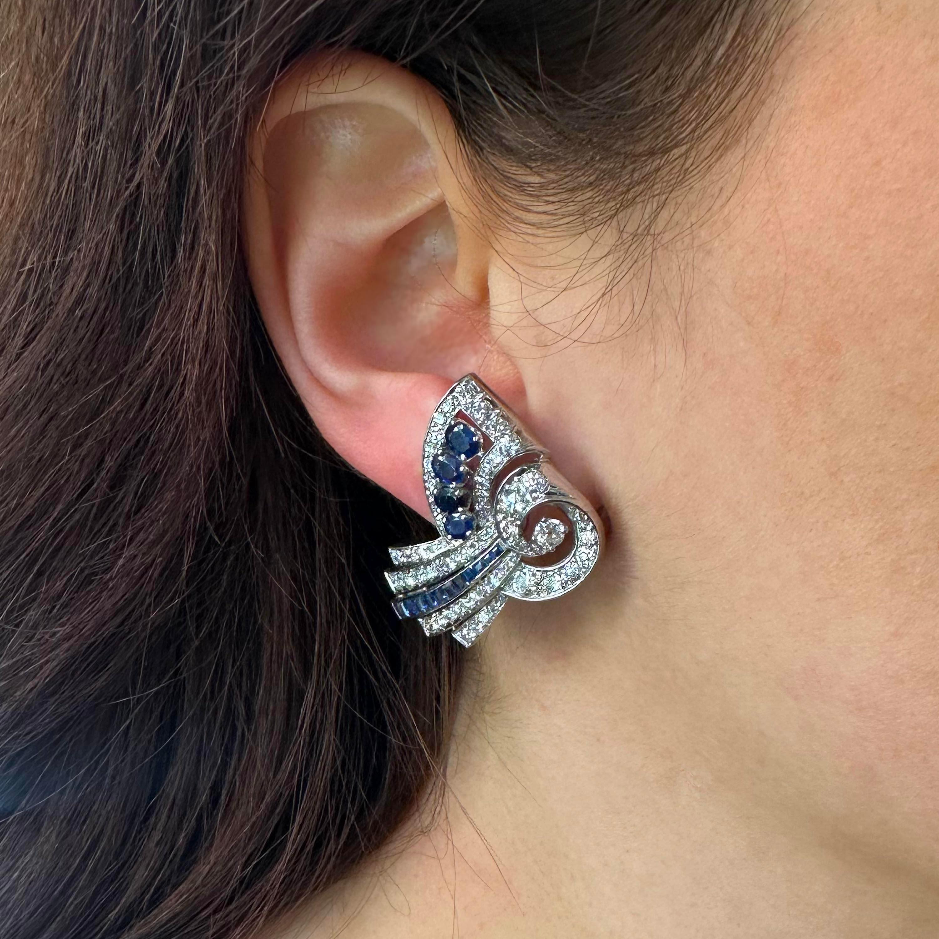 A pair of vintage, late Art Deco, sapphire, diamond and platinum earrings, with graduating oval faceted sapphires, in claw settings and old-cut and eight-cut diamonds in grain settings, in a stylised swirl, with a festoon of square calibré cut
