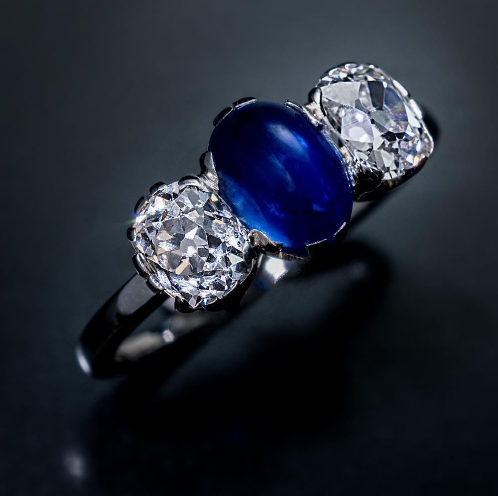 Circa 1925

This Art Deco era vintage platinum engagement ring is centered with a high-dome cabochon cut 1.88 ct sapphire of an excellent velvety blue color. The sapphire is flanked by two sparkling old cushion cut diamonds (I color, VS2 and SI1