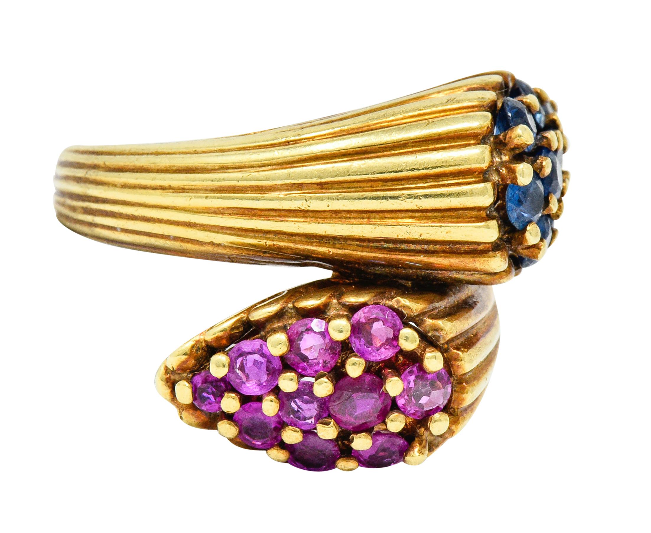 Bypass style ring is designed with a deeply fluted shank

That terminates as two pear shaped forms, nestled beside each other

Pavè set with round cut sapphires and rubies weighing in total approximately 1.82 carats

With medium-dark blue to blue