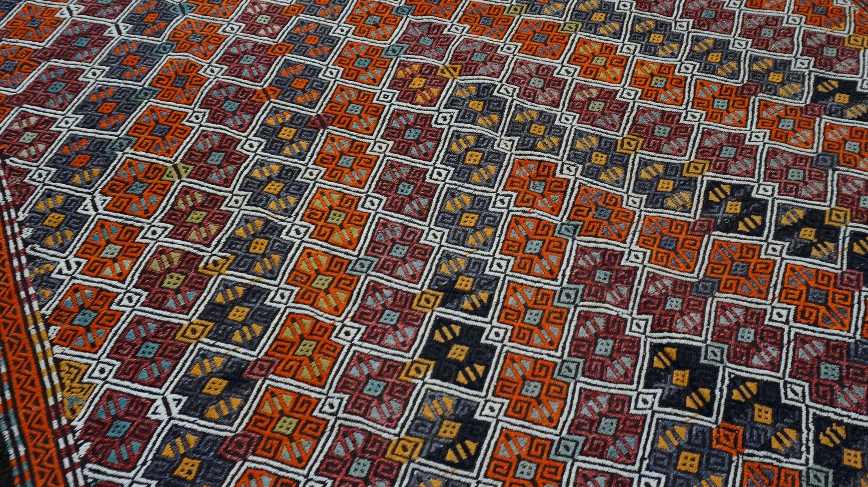 Dieser farbenfrohe, handgewebte Flachgewebe-Kelim ist ein beeindruckendes Beispiel für traditionelle Handwerkskunst mit komplizierten Stammesmotiven und leuchtenden Naturfarben. Dieses Vintage-Stück wurde aus handgesponnener Wolle hergestellt und