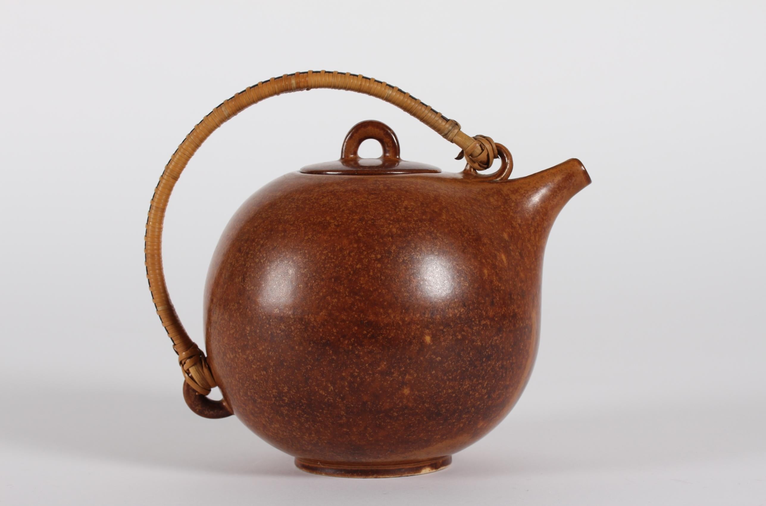 Globular ceramic teapot model no. 63 designed by the Danish ceramist Eva Stæhr Nielsen (1911-1976) and manufactured by Saxbo ceramic workshop

The teapot is decorated with glaze in yellow-brown ochre shades and has a bast handle 
Signed Saxbo II