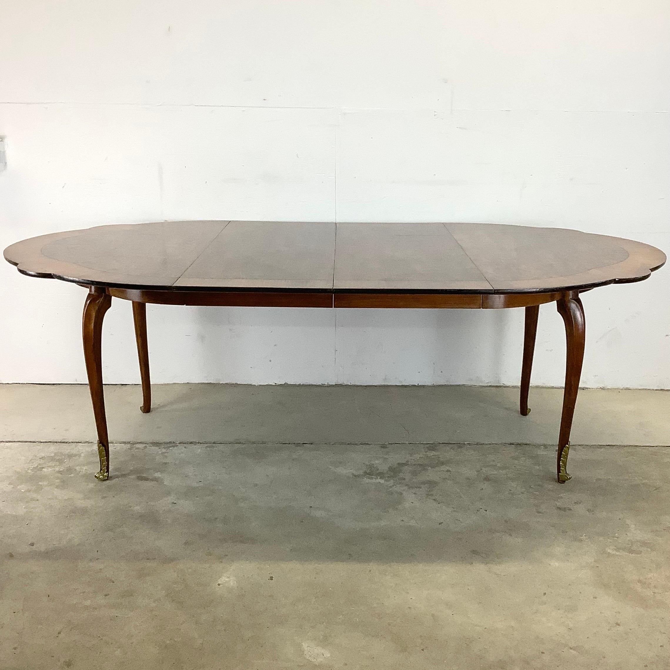 This unique vintage dining table features beautiful mixed wood finish with matching removable leaves that open it from a round dining table to a long oval dining table. The unique scalloped edge detail, tapered legs, and the detailed cast metal foot