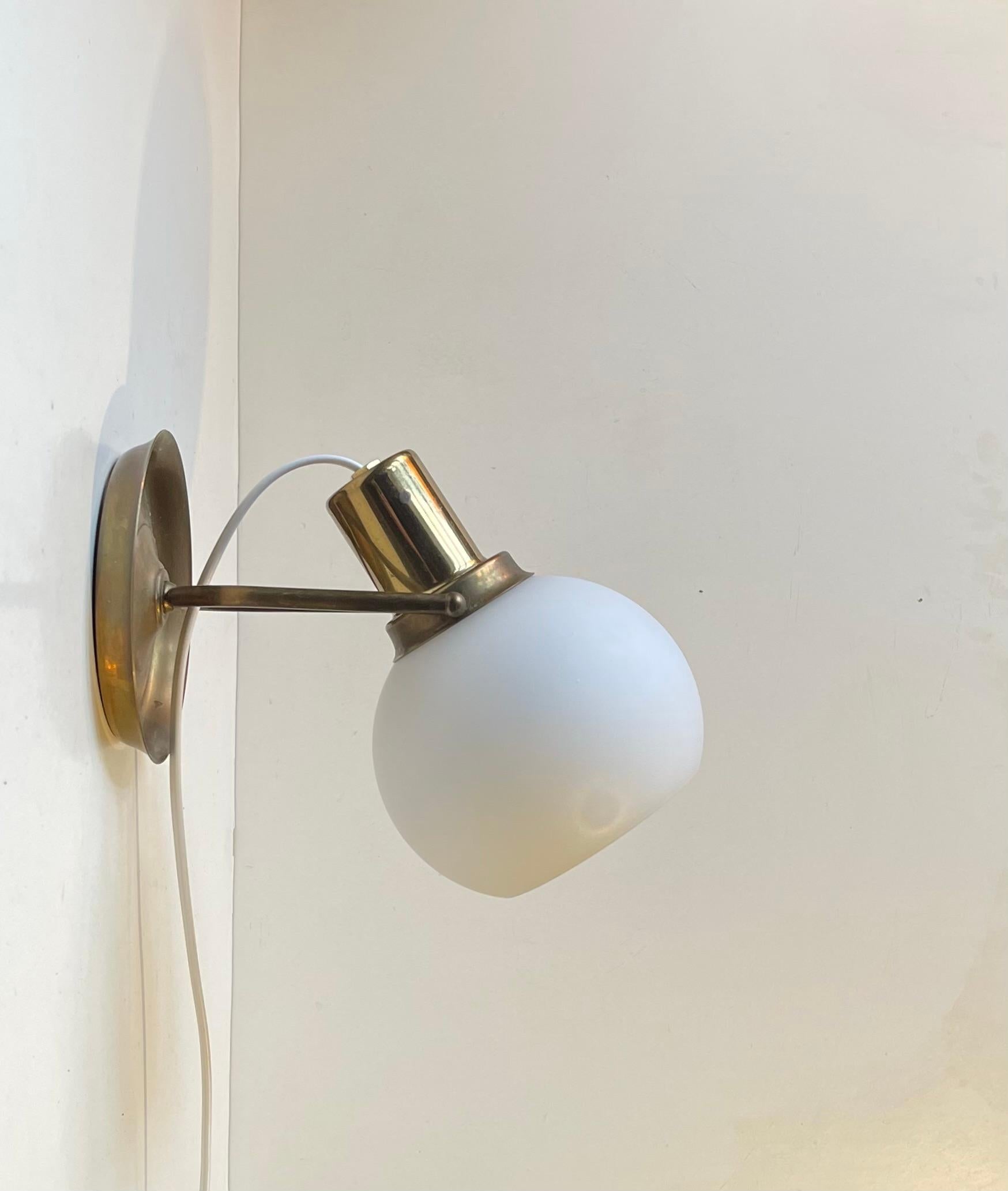 Cette applique murale élégante en laiton patiné est dotée d'un abat-jour en verre opalin sphérique dépoli. Fabricant/designer scandinave inconnu dans le style de Fritz Schlegel et Vilhelm Lauritzen. Il est réglable en hauteur et en profondeur au