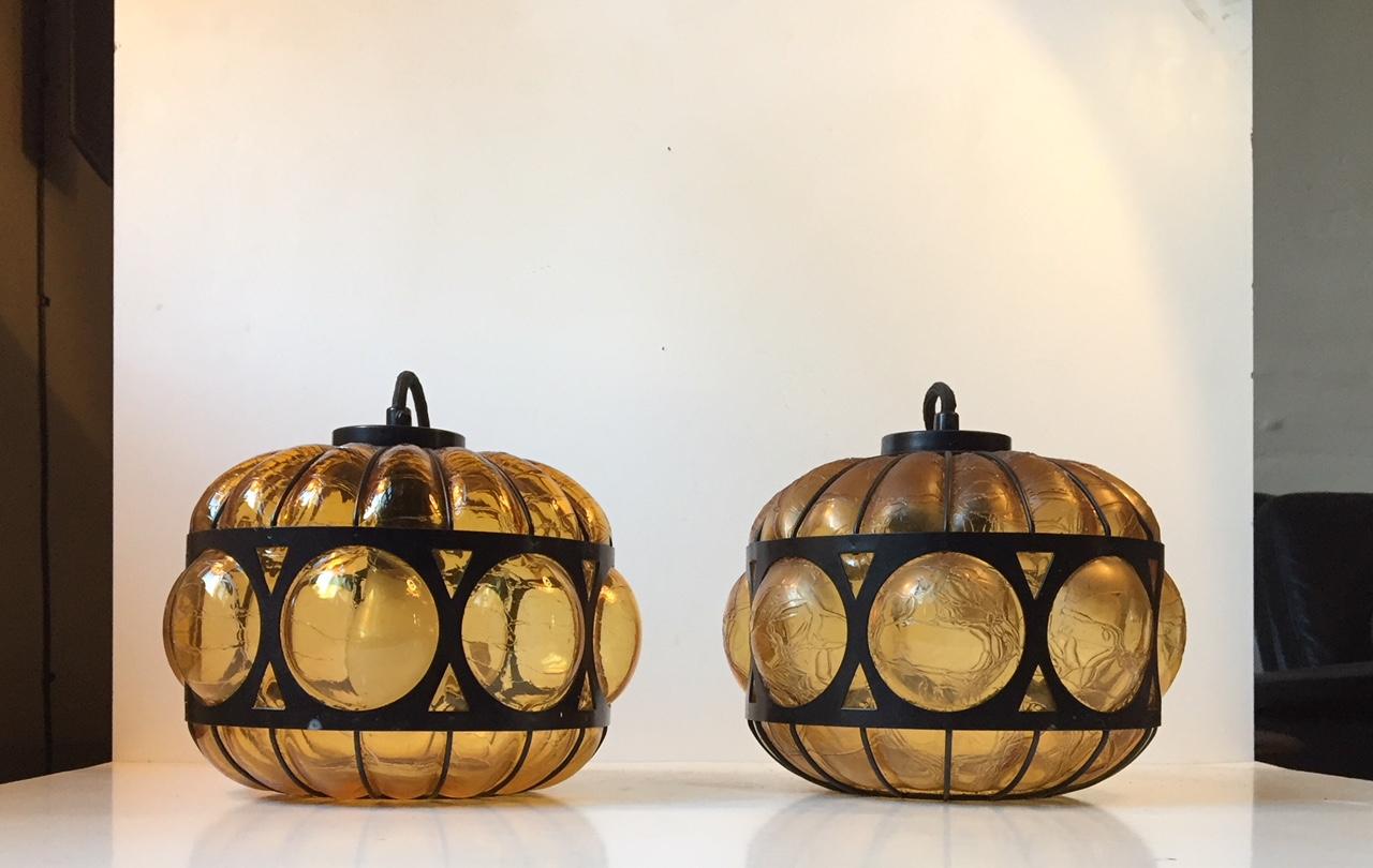 This set consists of 2 caged hand blown amber glass pendant lights. The glass displays texture and the steel 'cage' is powder coated black. It was manufactured in Scandinavia during the 1960s or 1970s in a style reminiscent of Seguso and Nanny