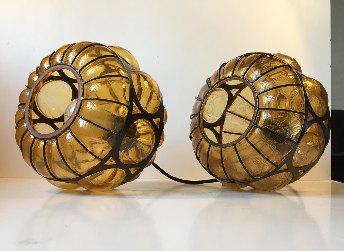 A set of 2 caged hand blown amber glass pendant lights. The glass technique applied resembles broken/shattered glass. The steel 'cage' is powder coated black. It was manufactured in Scandinavia during the 1960s or 1970s in a style reminiscent of