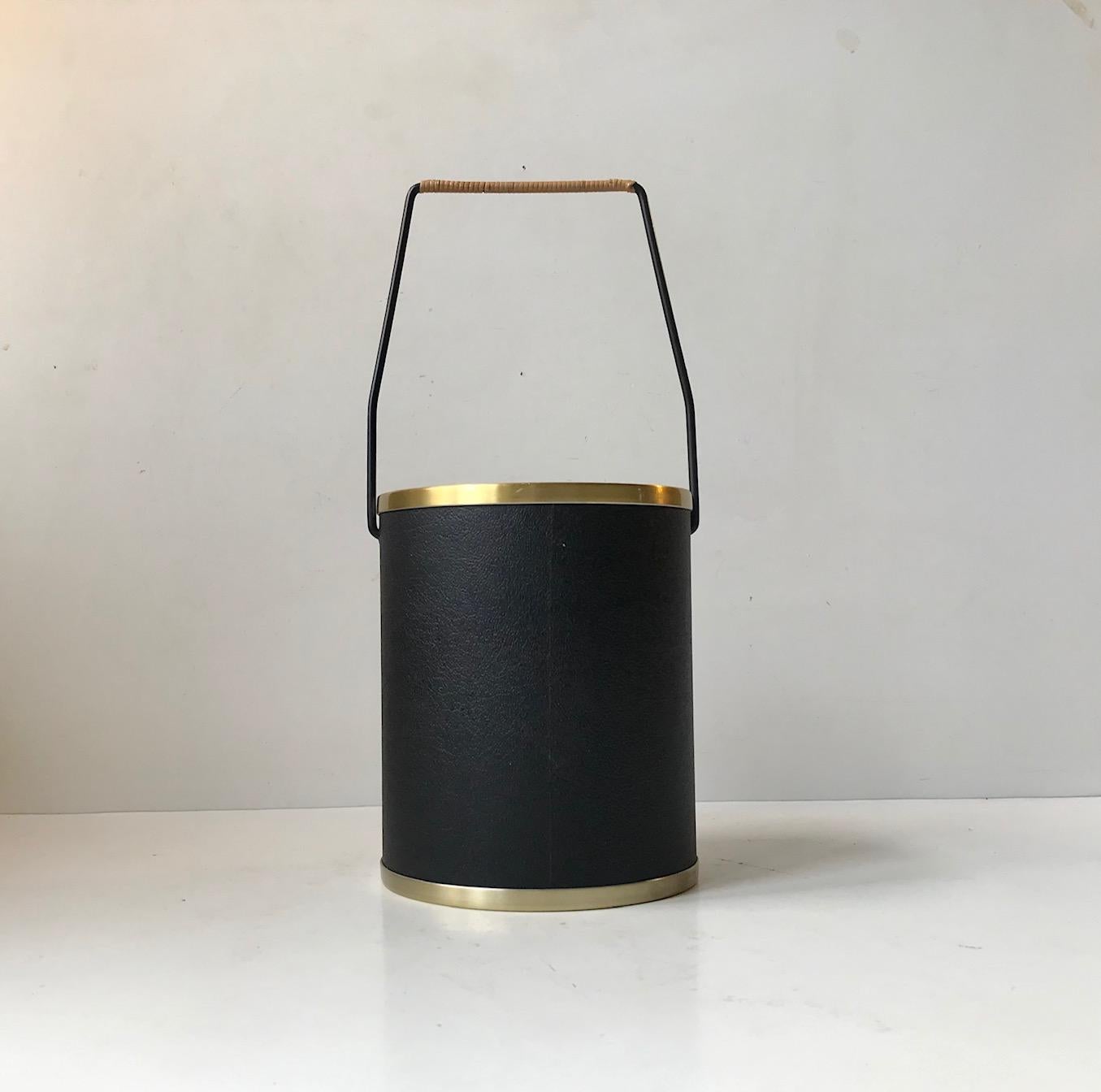 A stylized 1960s wine or champagne cooler. It is executed in brass-alloy aluminium, faux black leather and has a steel handle with rattan work. The sides features a thermos inlay so no ice is required to keep it cool. 
It was designed and